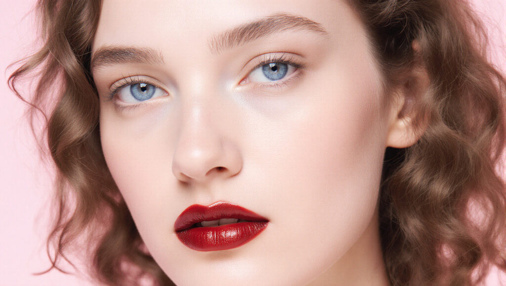 Close-Up Portrait of Woman with Curly Hair and Red Lipstick on Pink Background