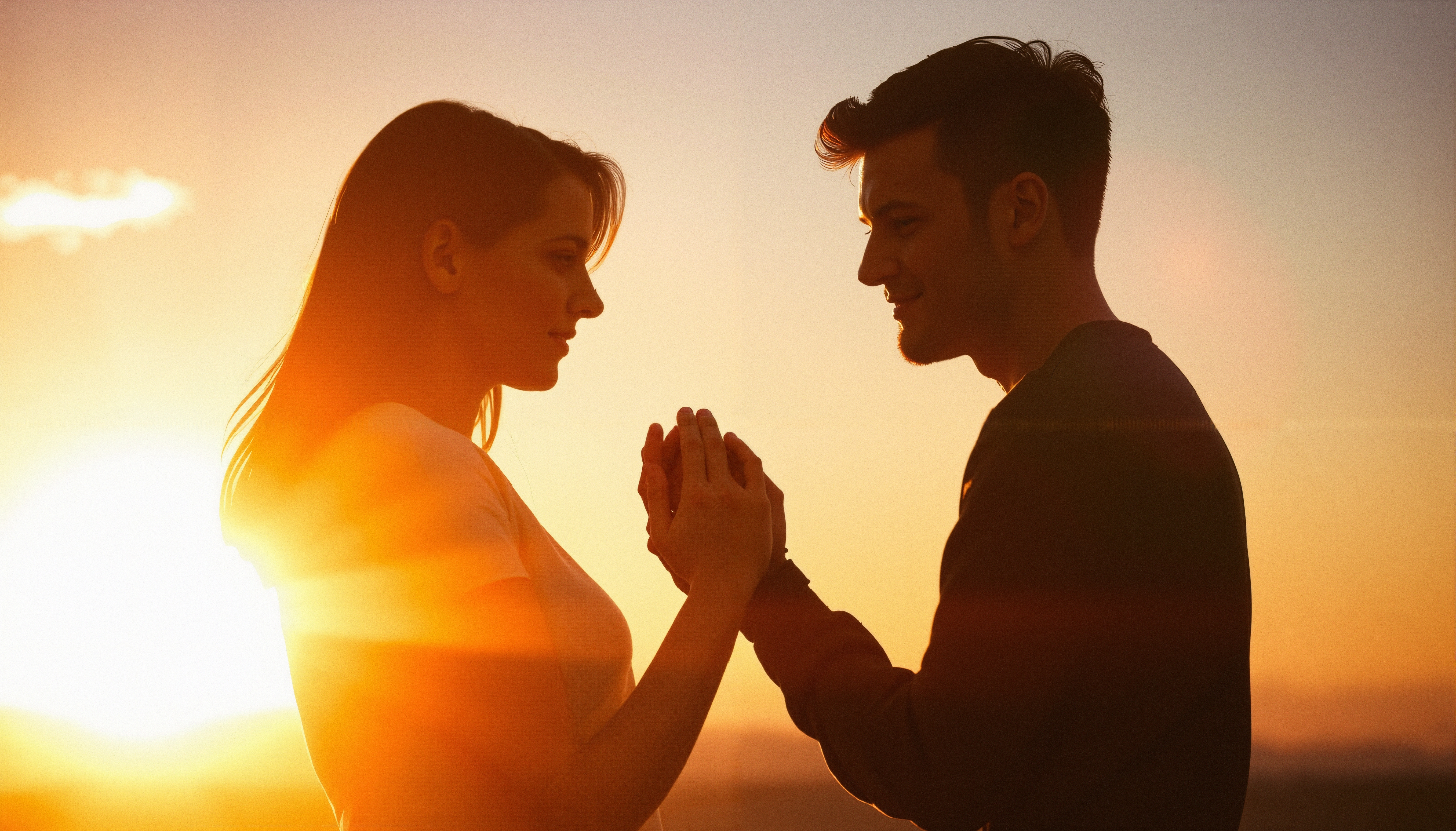 A couple holds hands at sunset, their silhouettes illuminated by the golden light, embodying romance and connection.