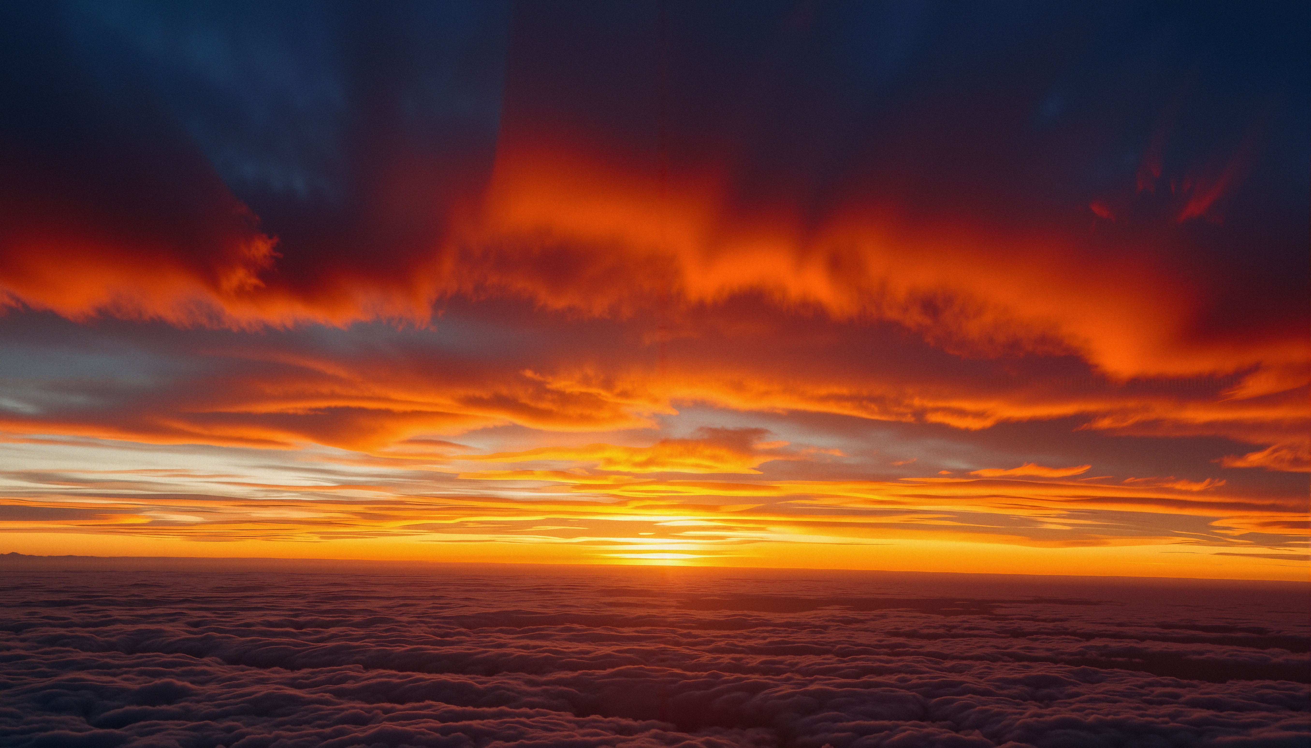 A stunning sunset with vibrant orange and red hues over a cloud-filled horizon, creating a dramatic and peaceful landscape.