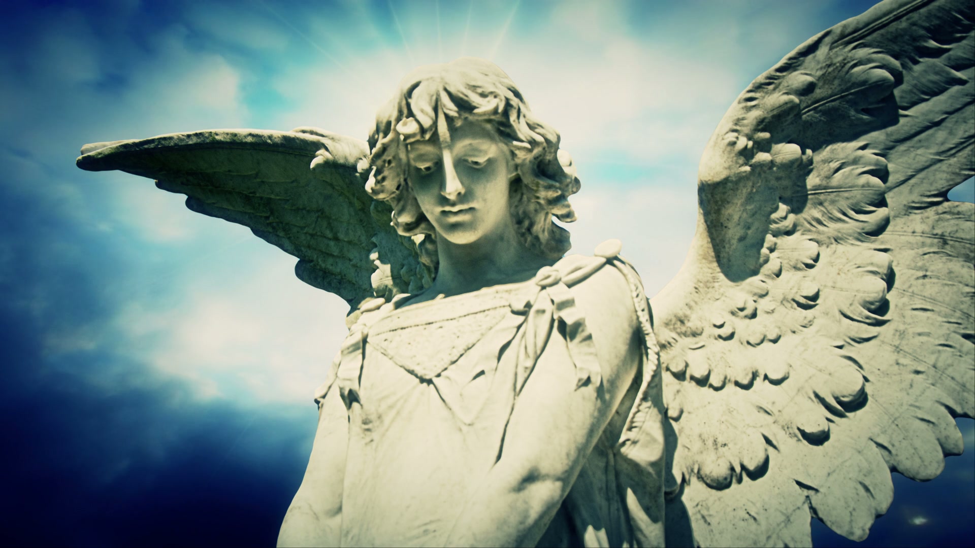 Majestic angelic statue with intricate wings bathed in sunlight against a time-lapse cloudy sky, symbolizing peace and spirituality.