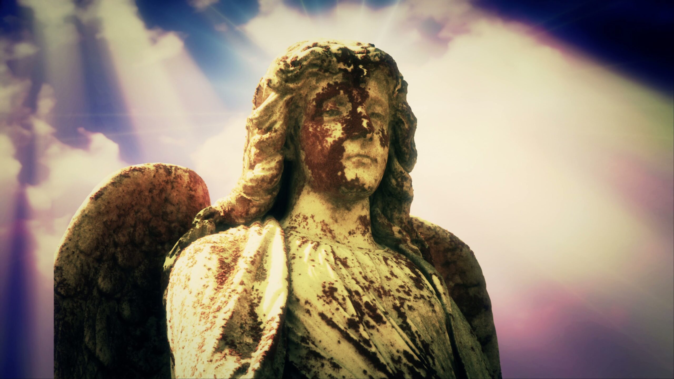 4K video loop of a weathered angel statue with sunlight and a colorful time-lapse sky.