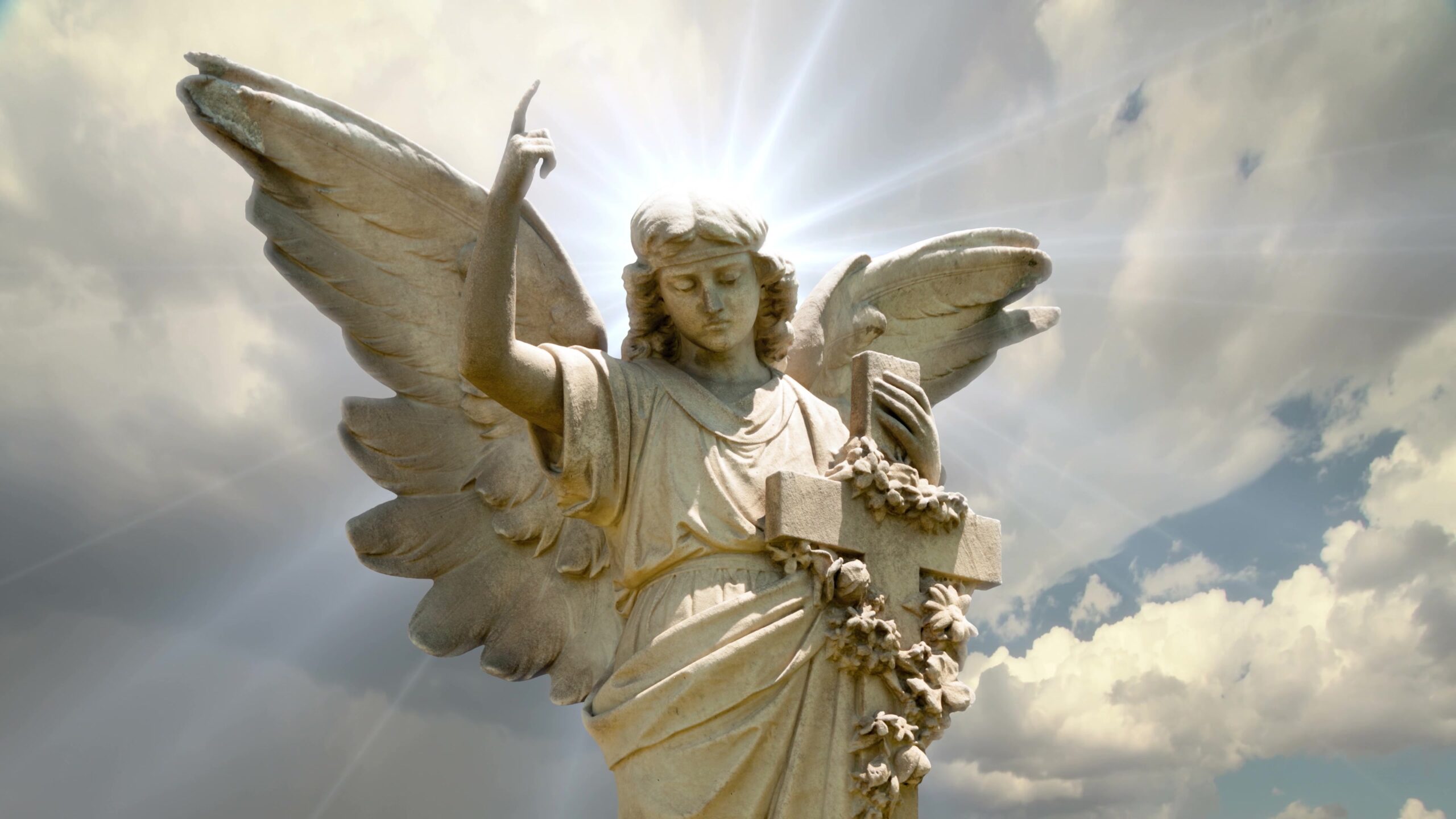 A 4K video loop of a majestic stone angel statue holding a cross under a radiant sky.
