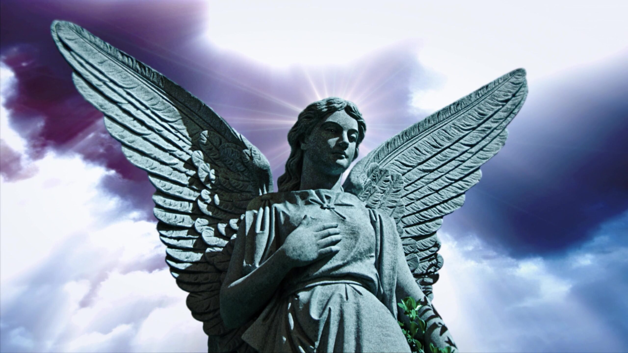 4K video loop of a stone angel statue with outstretched wings against a dramatic, cloudy sky with rays of light.