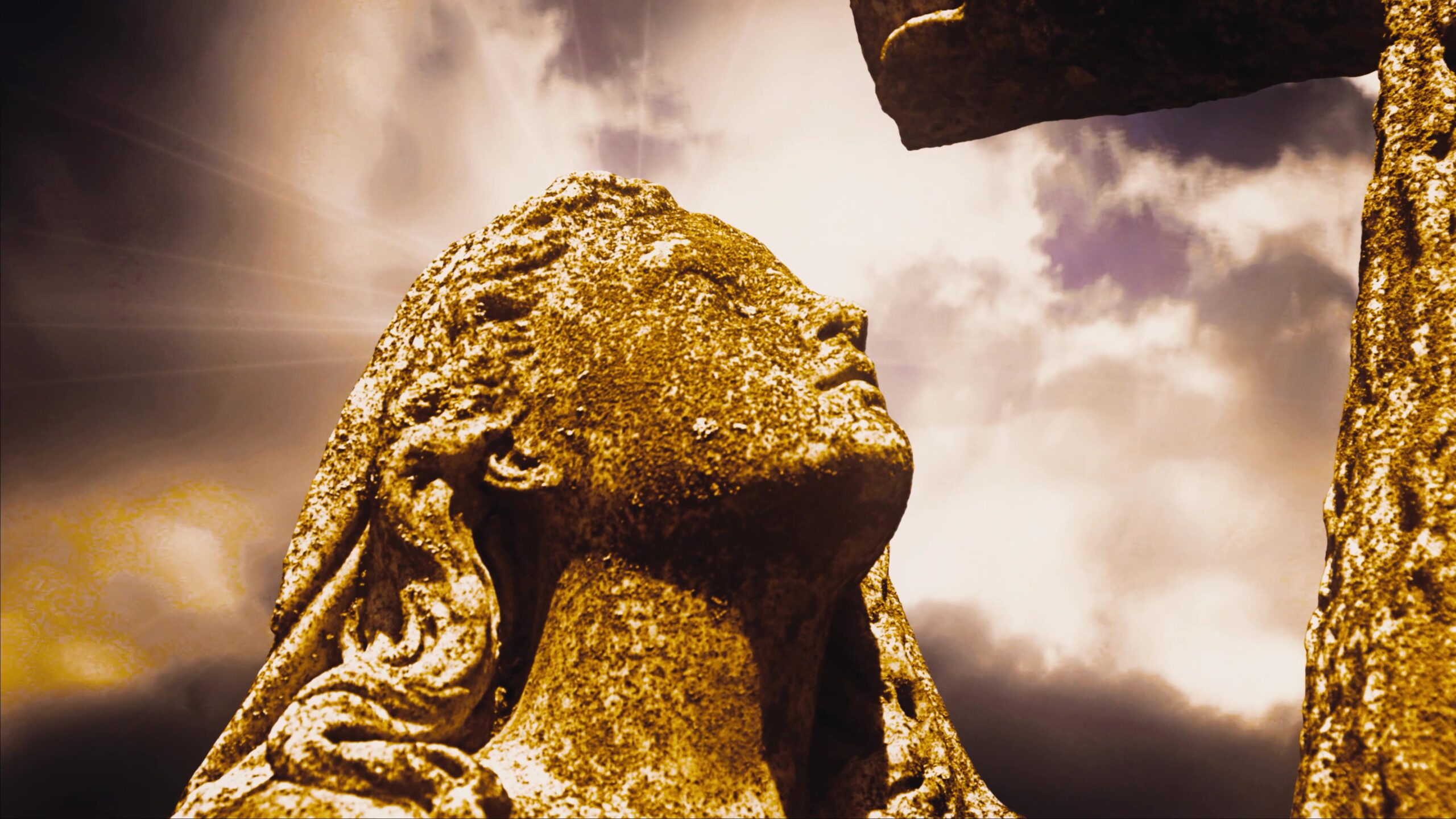4K video loop of a stone sculpture of a woman gazing upwards under a dramatic cloud-filled, time-lspse sky with light beams.