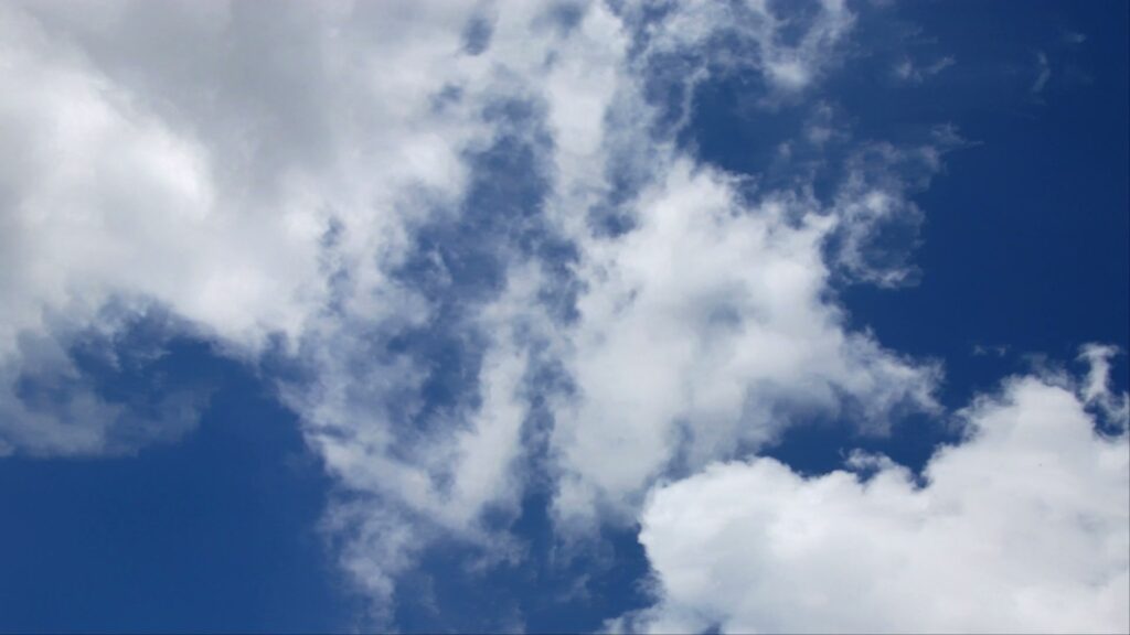 A serene sky filled with fluffy white time-lapse clouds against a vibrant blue backdrop, conveying tranquility and vastness.
