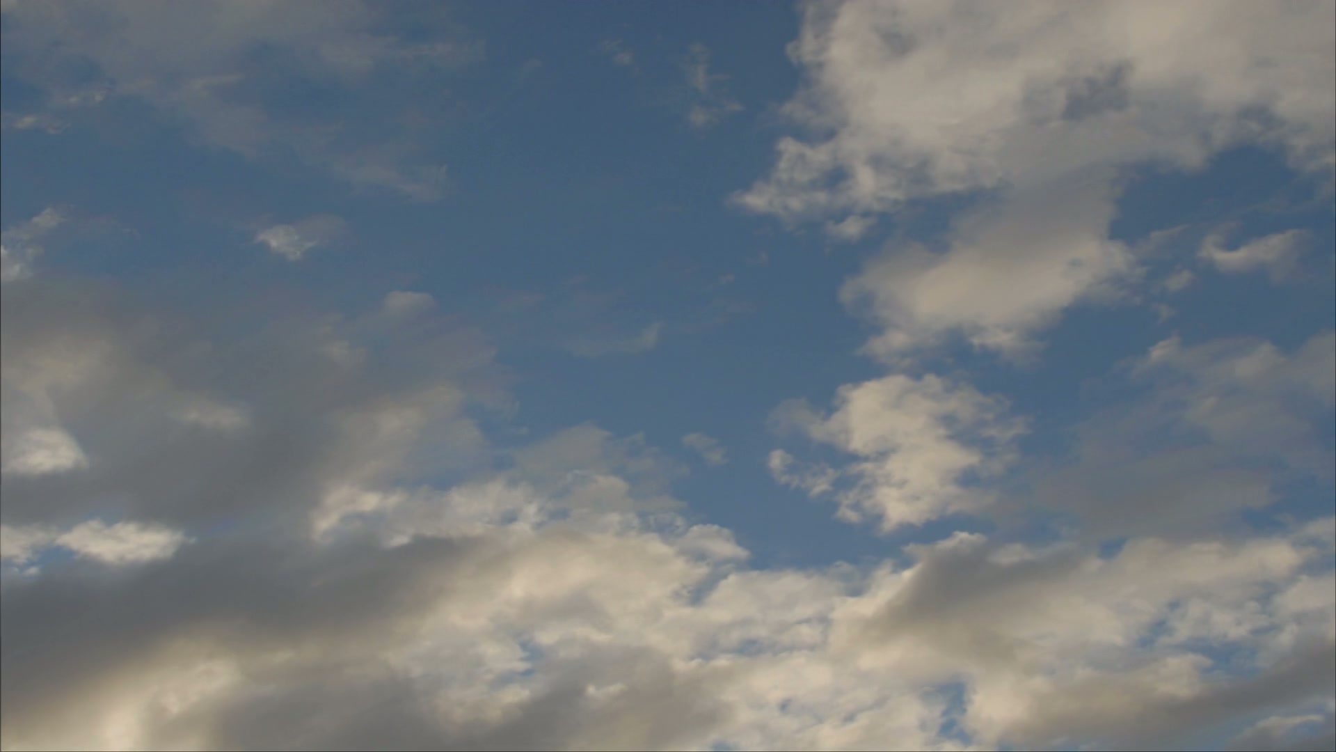 A serene view of a time-lapse cloudy sky featuring fluffy white and gray clouds against a vibrant blue background, exuding tranquility and natural beauty.