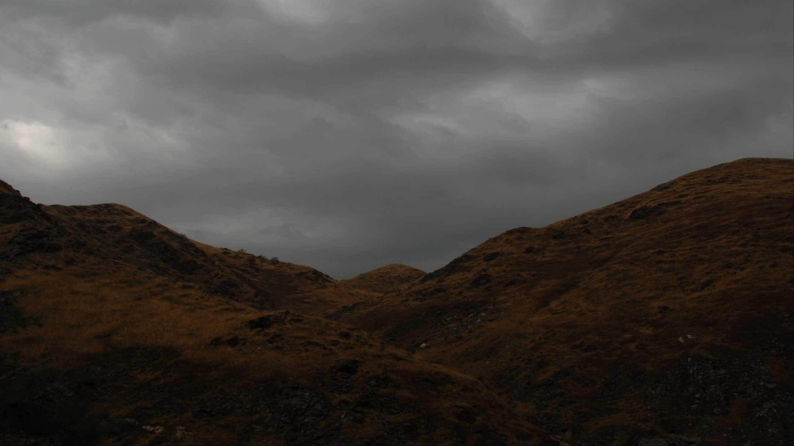4K video of rolling hills under a dramatic overcast sky with earthy tones and dark time-lapse clouds.