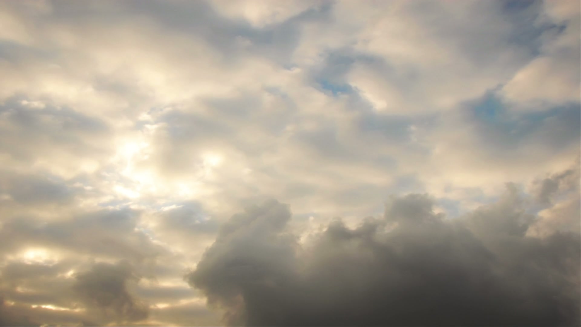 A dramatic evening sky filled with a mix of light and dark time-lapse clouds, with sunlight peeking through, creating a dynamic and serene atmosphere.