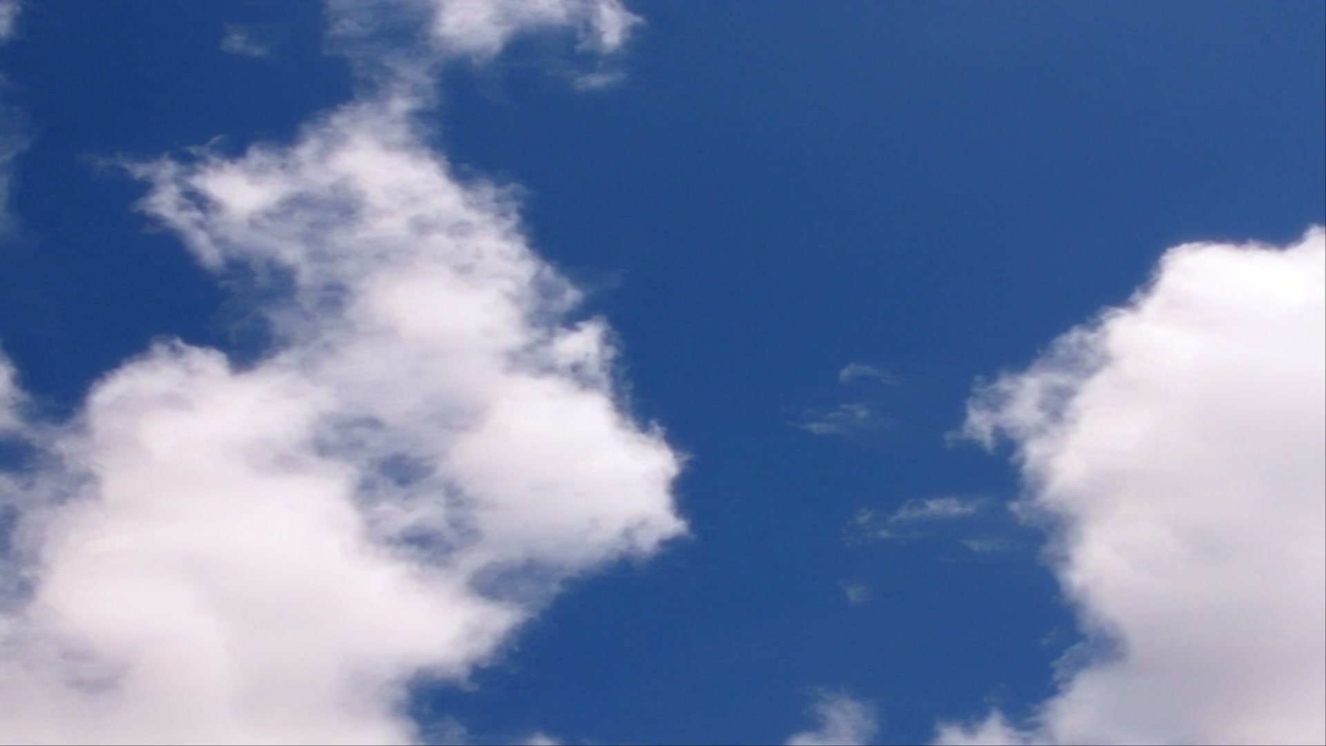 A vibrant blue sky filled with fluffy white time-lapse clouds, creating a serene and peaceful atmosphere as sunlight highlights their soft texture.