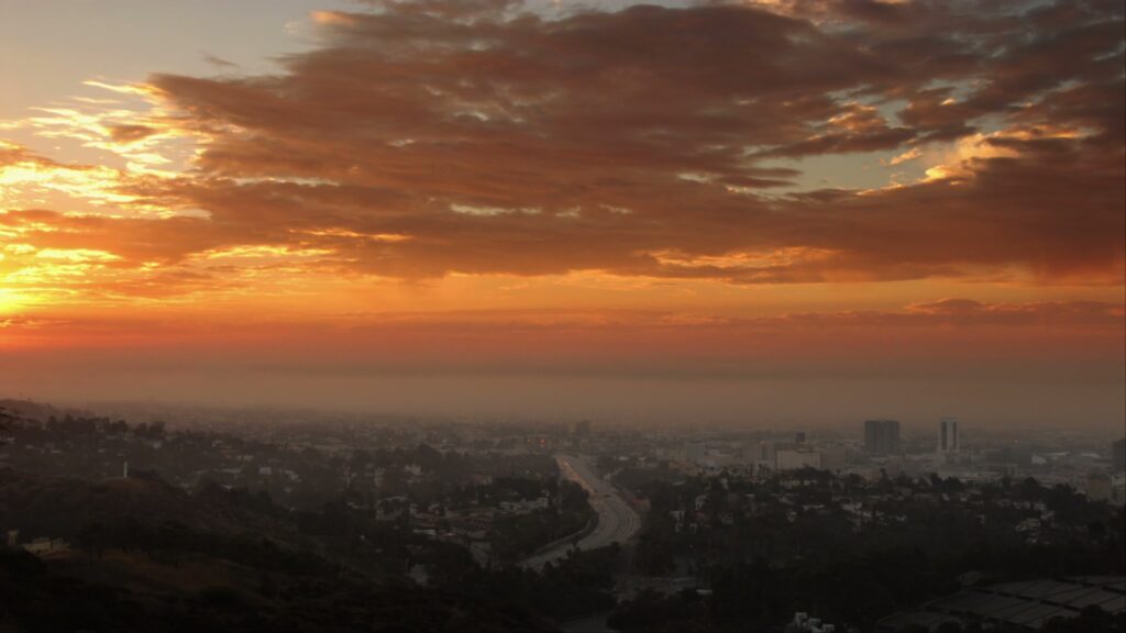 A breathtaking time-lapse sunset casts an golden orange glow over a sprawling cityscape, featuring silhouettes of buildings and a prominent road leading into the urban horizon, creating a serene and tranquil evening scene.