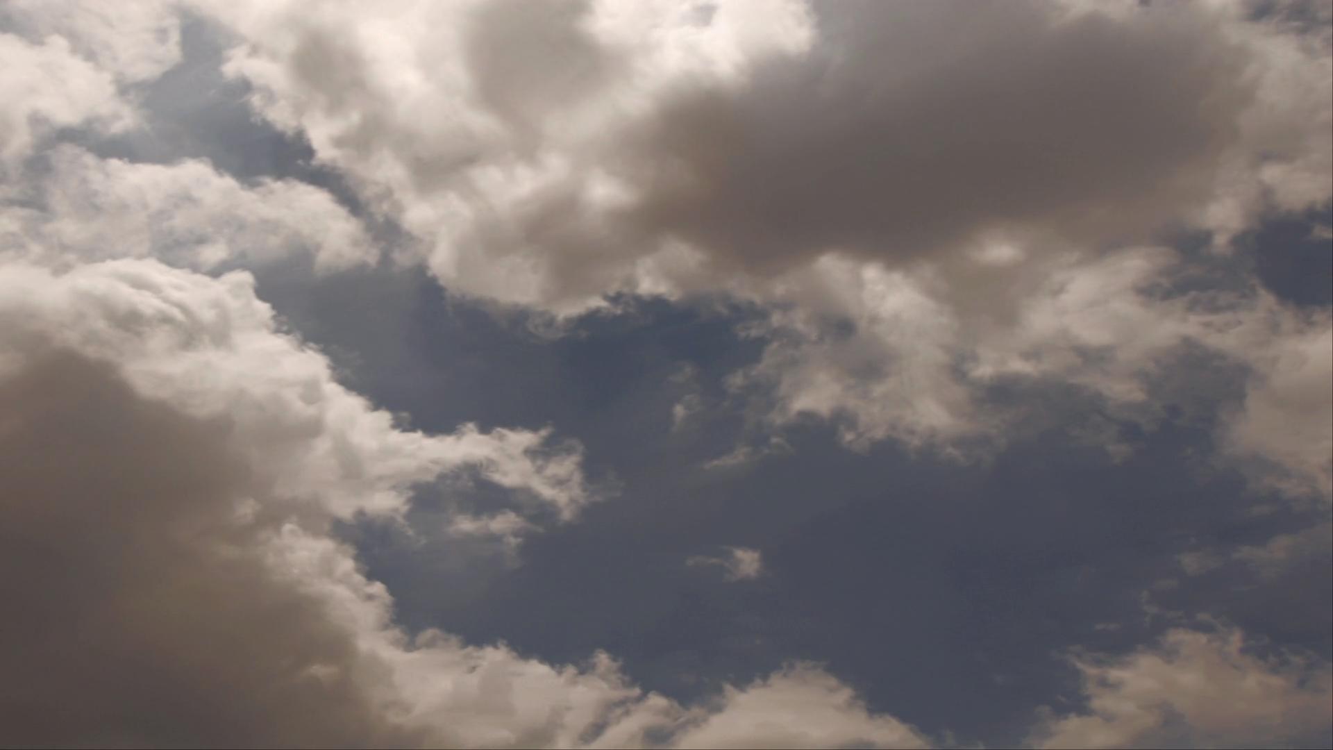 Time-lapse storm clouds gather in a dramatic sky with a small patch of blue visible, creating a striking contrast and highlighting the atmospheric tension.