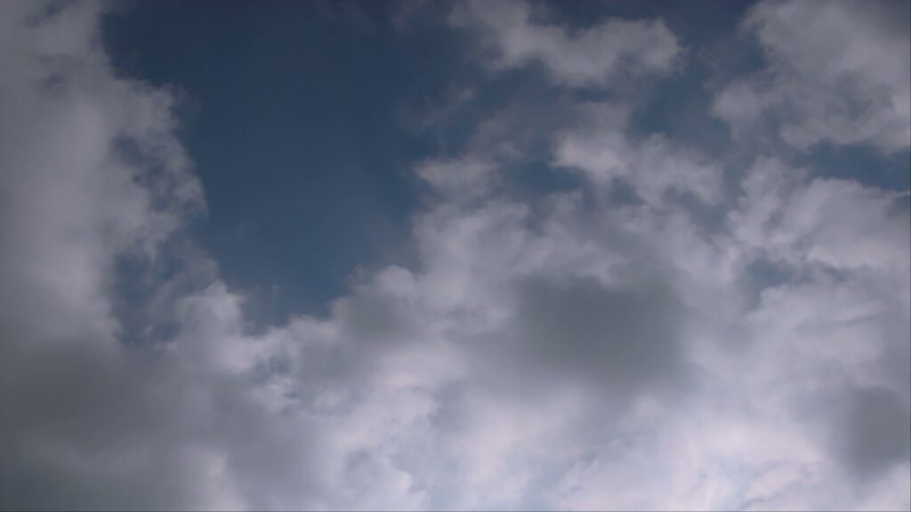 A tranquil sky with fluffy, wispy white time-lapse clouds spread across a rich blue background, creating a serene and peaceful atmosphere.