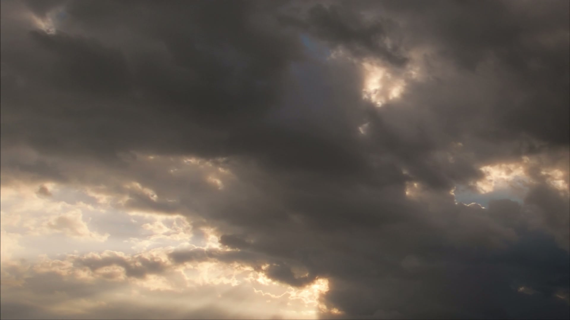 A dramatic sky filled with dark, dense time-lapse clouds, with rays of sunlight breaking through, showcasing a dynamic contrast between light and shadow, highlighting the textures and depth of the cloud formations.