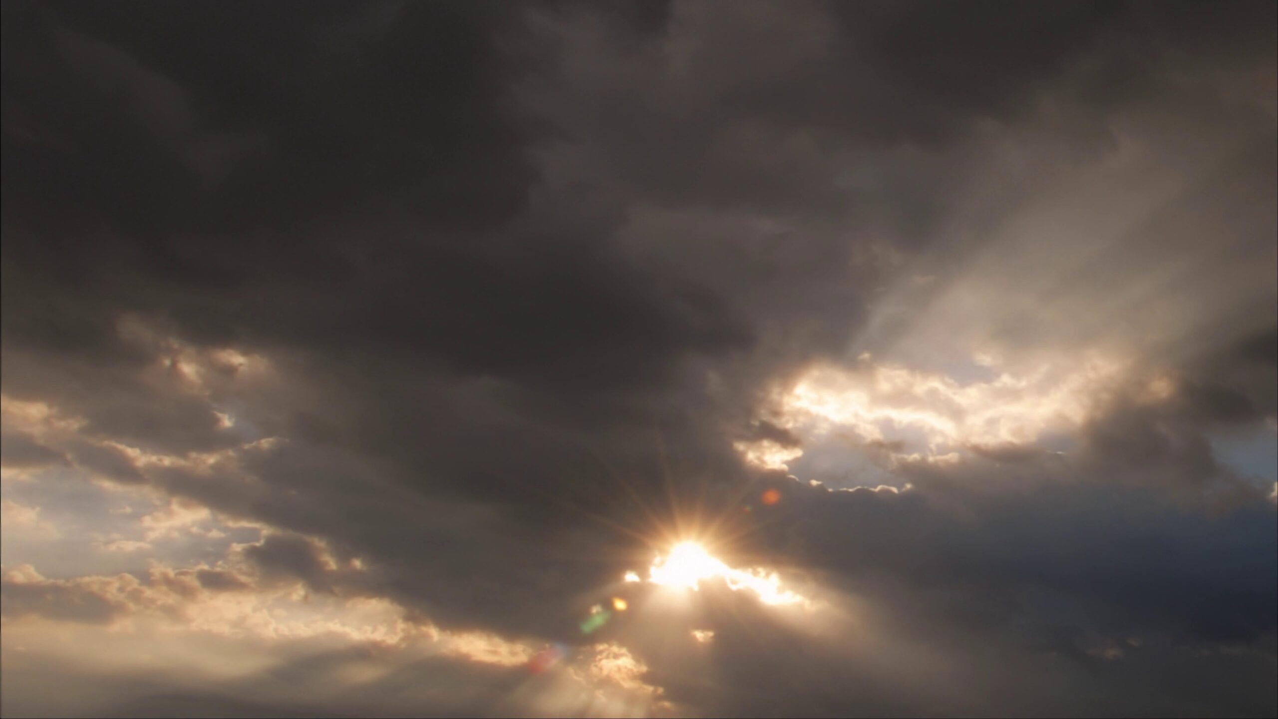 Dramatic 4K video sky with dark time-lapse storm clouds and rays of sunlight filtering through, creating a contrast between shadow and light.