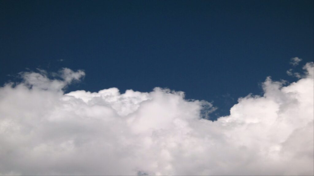 A serene landscape depicting a deep blue sky adorned with puffy white time-lapse clouds, creating a peaceful and expansive atmosphere.