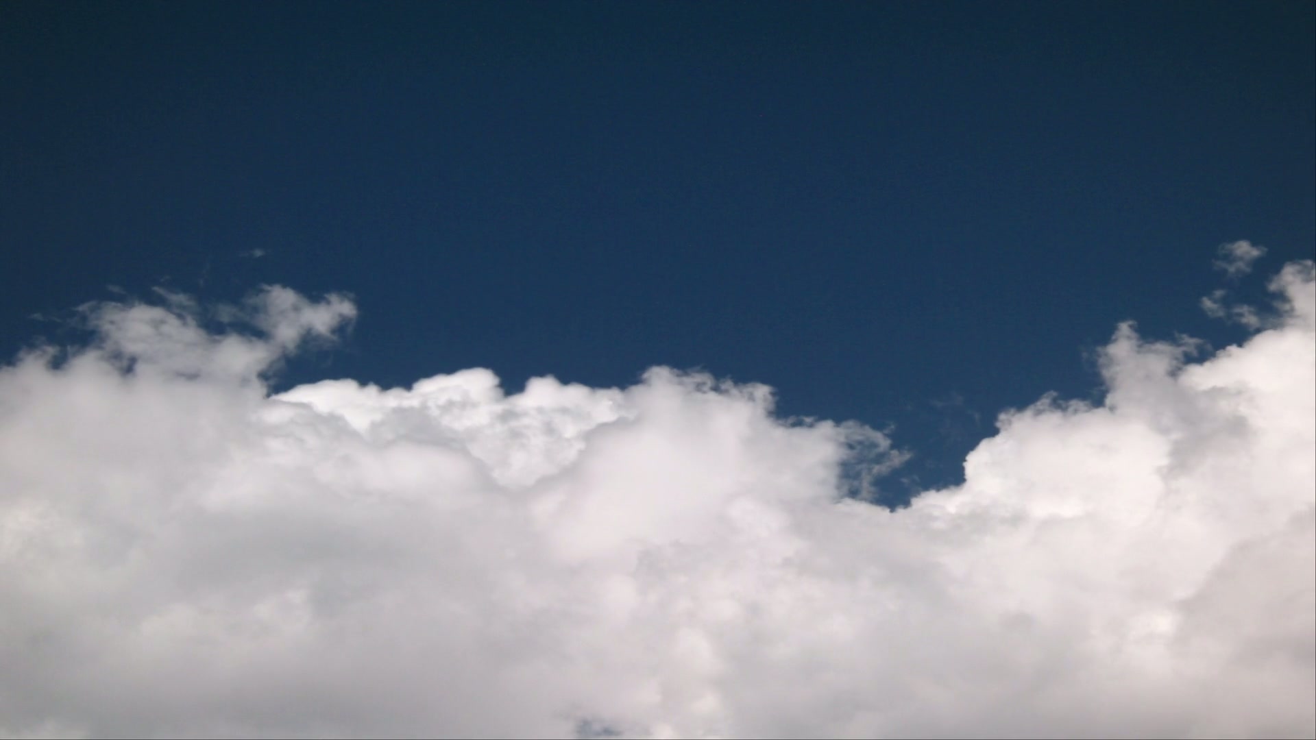 A serene landscape depicting a deep blue sky adorned with puffy white time-lapse clouds, creating a peaceful and expansive atmosphere.