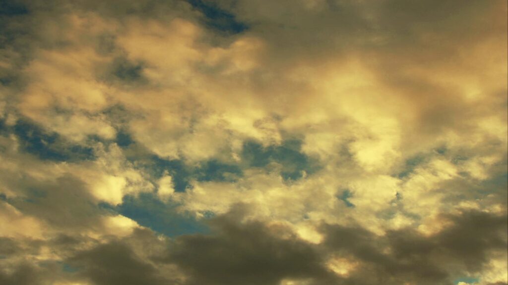 Serene sky filled with drifting white time-lapse clouds glowing under sunset sunbeams