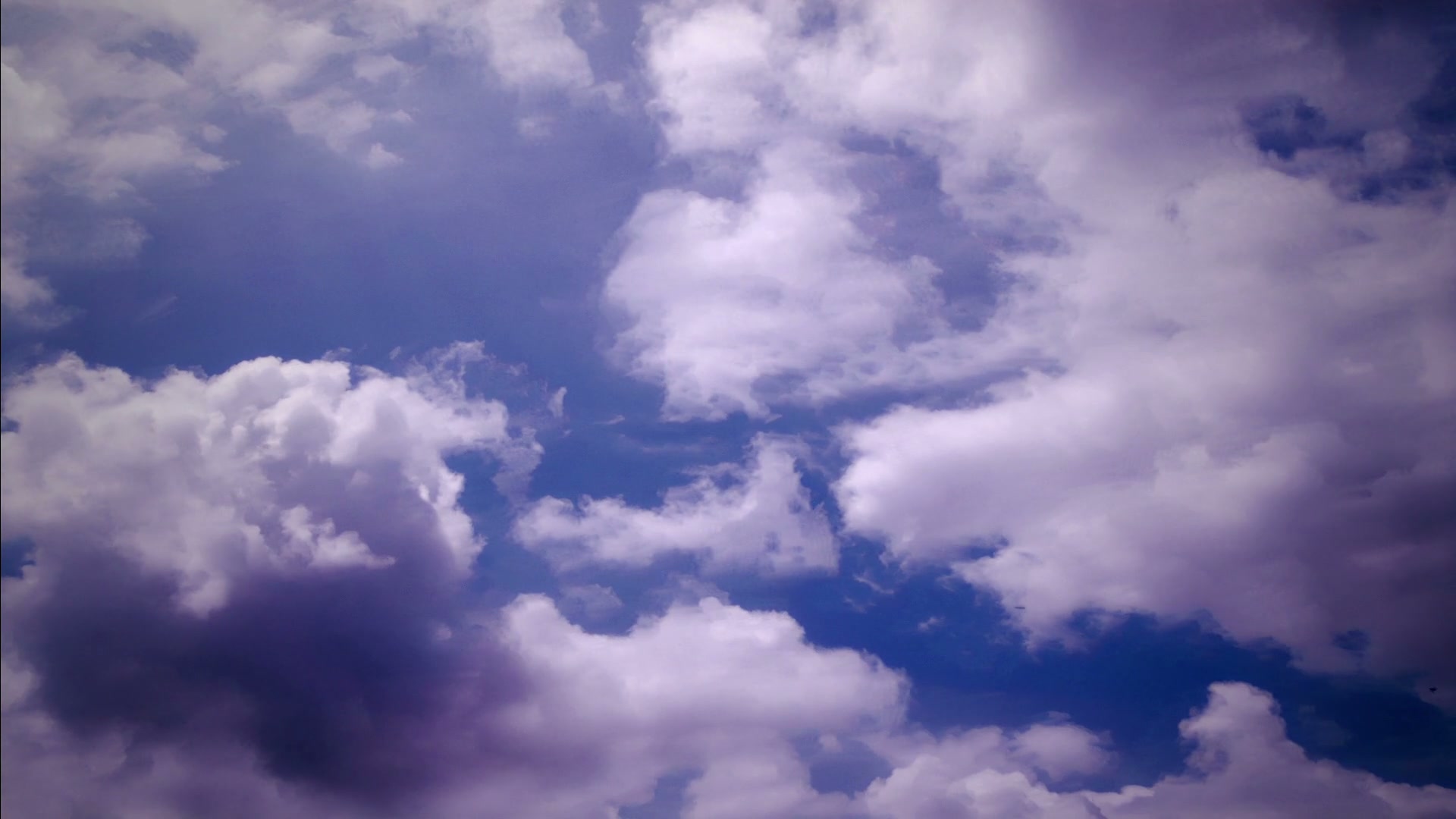 A vibrant sky filled with fluffy, white time-lapse clouds against a deep blue background.