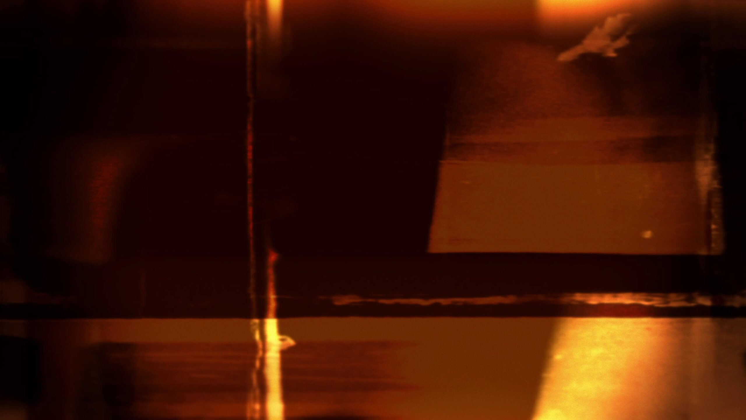 4K video loop of grainy 16mm film leader glowing warmly under dim lighting.