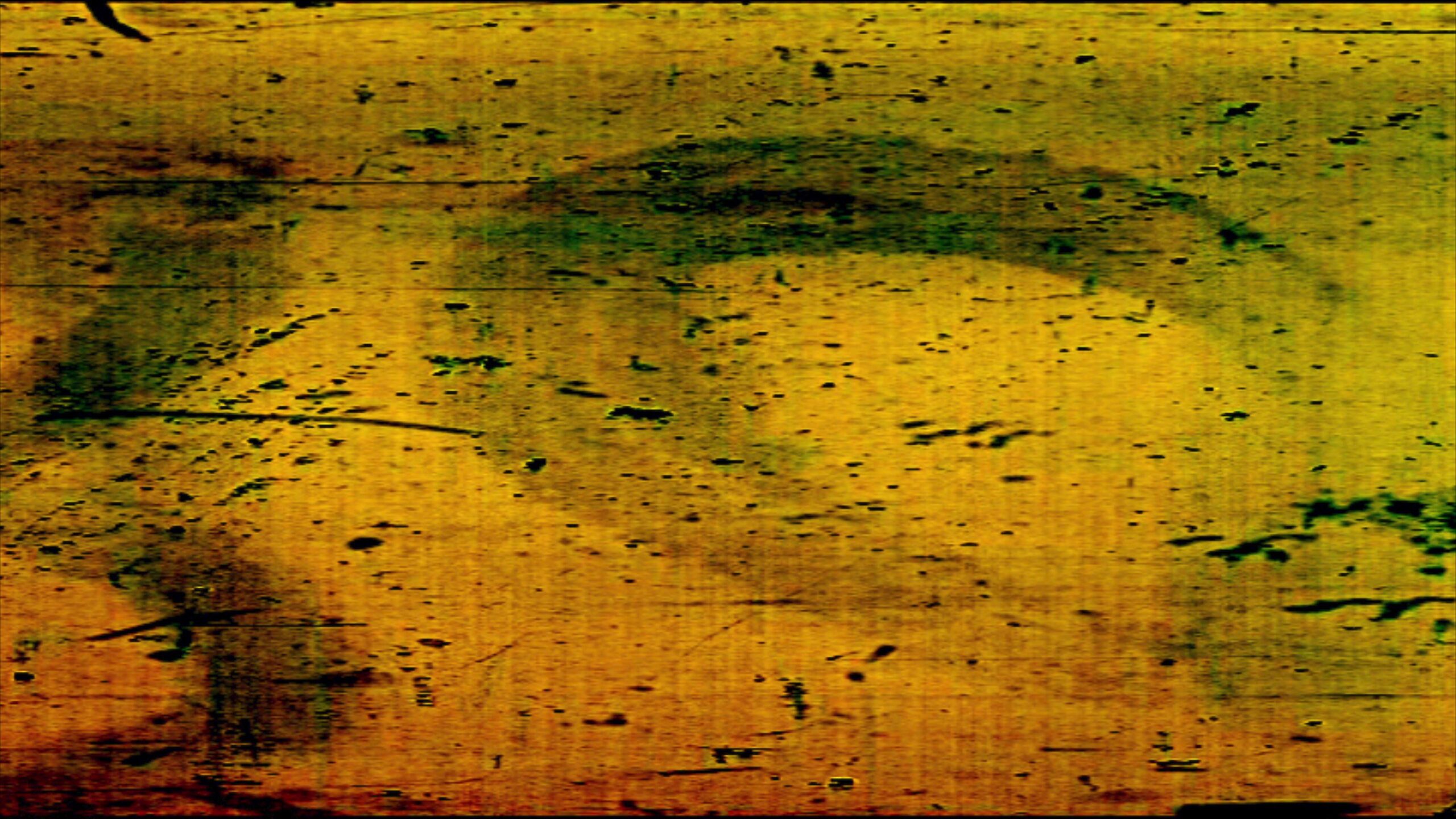 A distressed 4K video loop of 16mm film leader with scratches, grain, and aged emulsion texture in warm yellow and green tones.