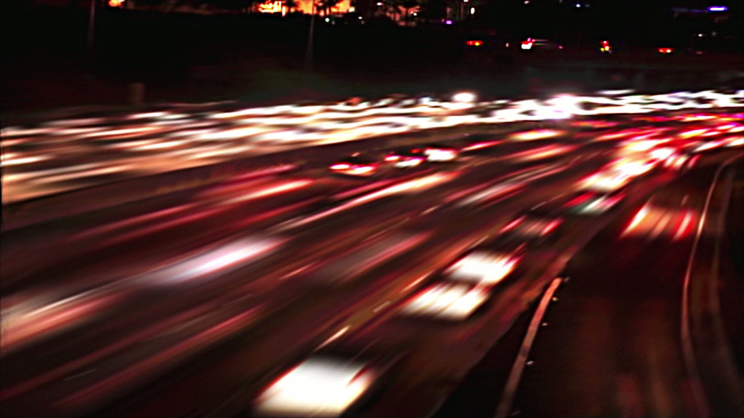 4K video loop of a nighttime highway with blurred light trails from moving traffic, showcasing headlight and taillight patterns in dynamic, vibrant lines.