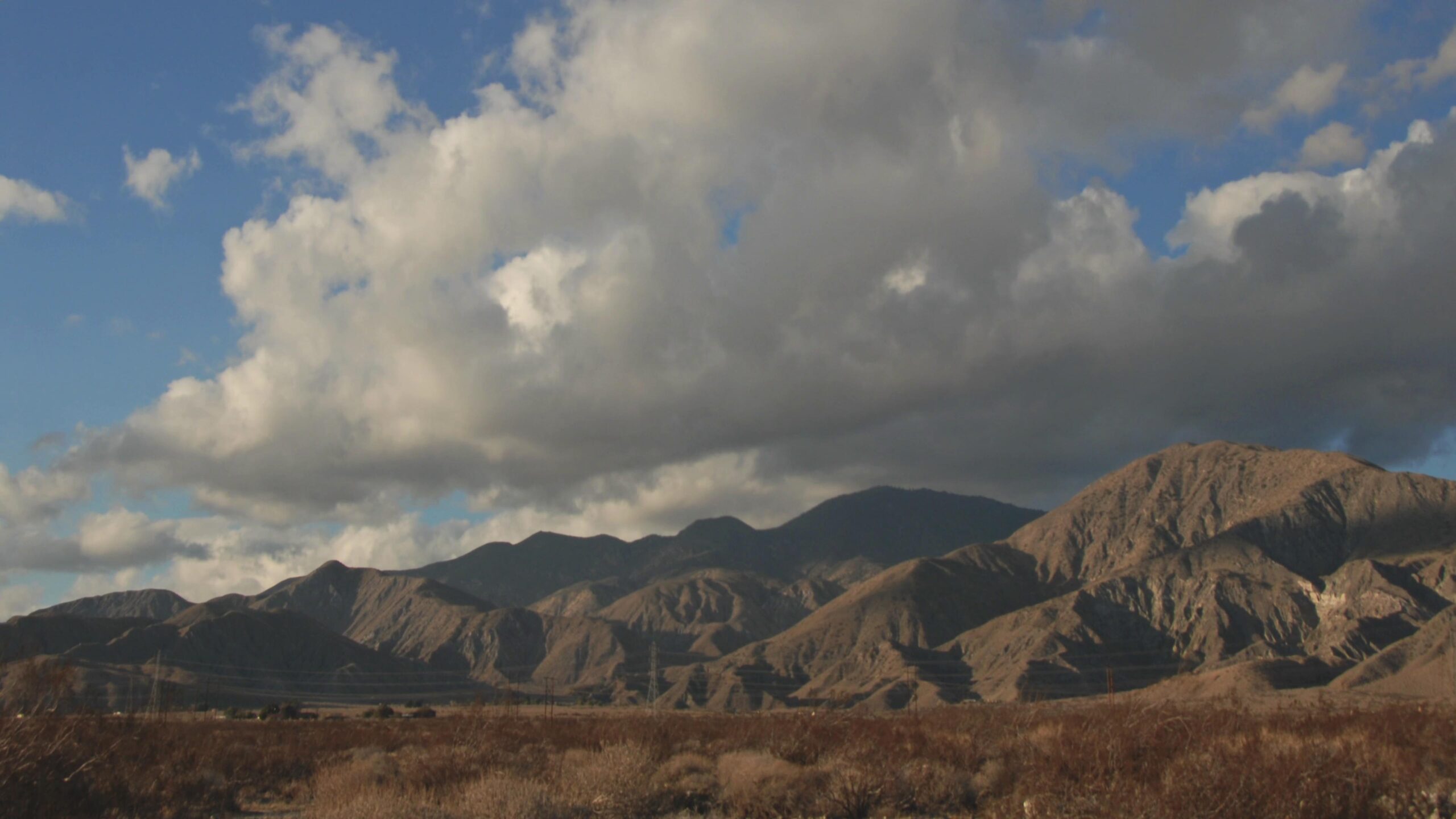 A stunning 4k video view of mountains under a time-lapse cloudy sky, with dry terrain below.