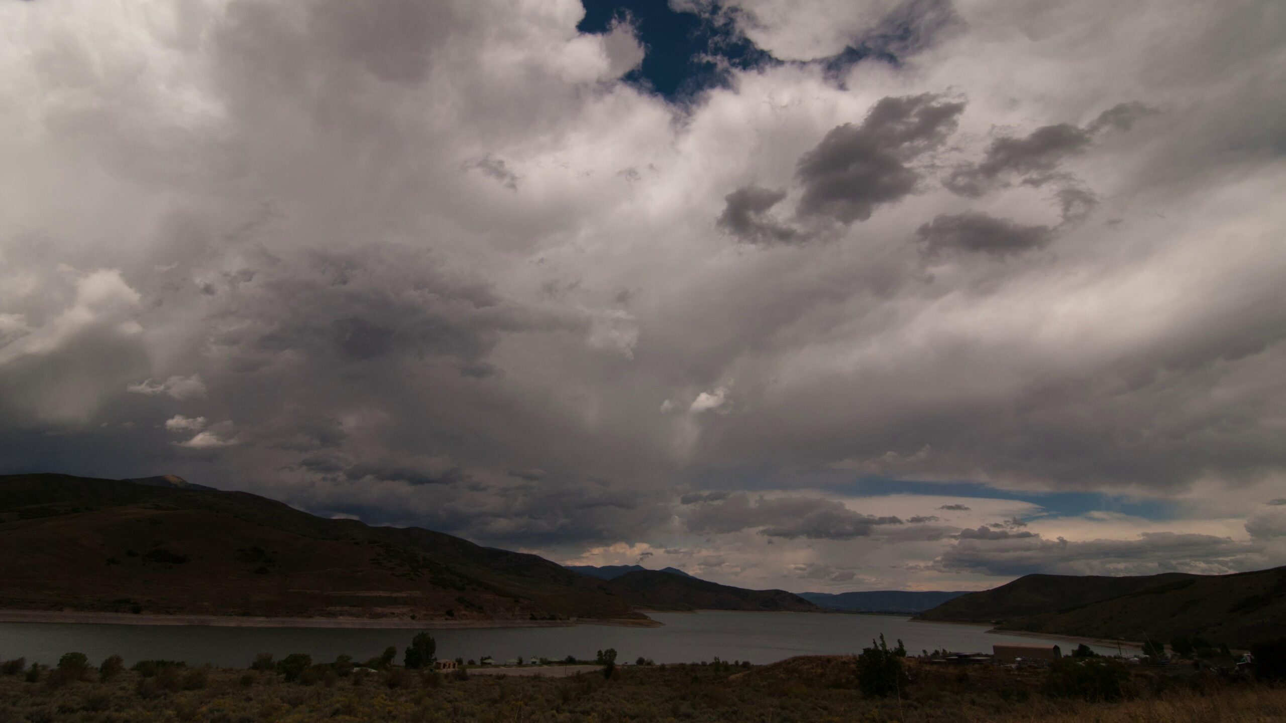 Expansive 4K video landscape with stormy time-lapse clouds over a reservoir and hills.