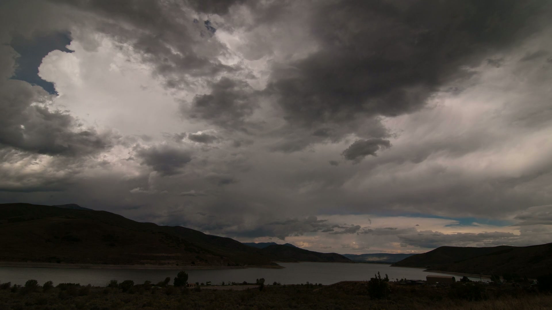A dramatic time-lapse sky filling with dark, brooding storm clouds reflect over a lake.