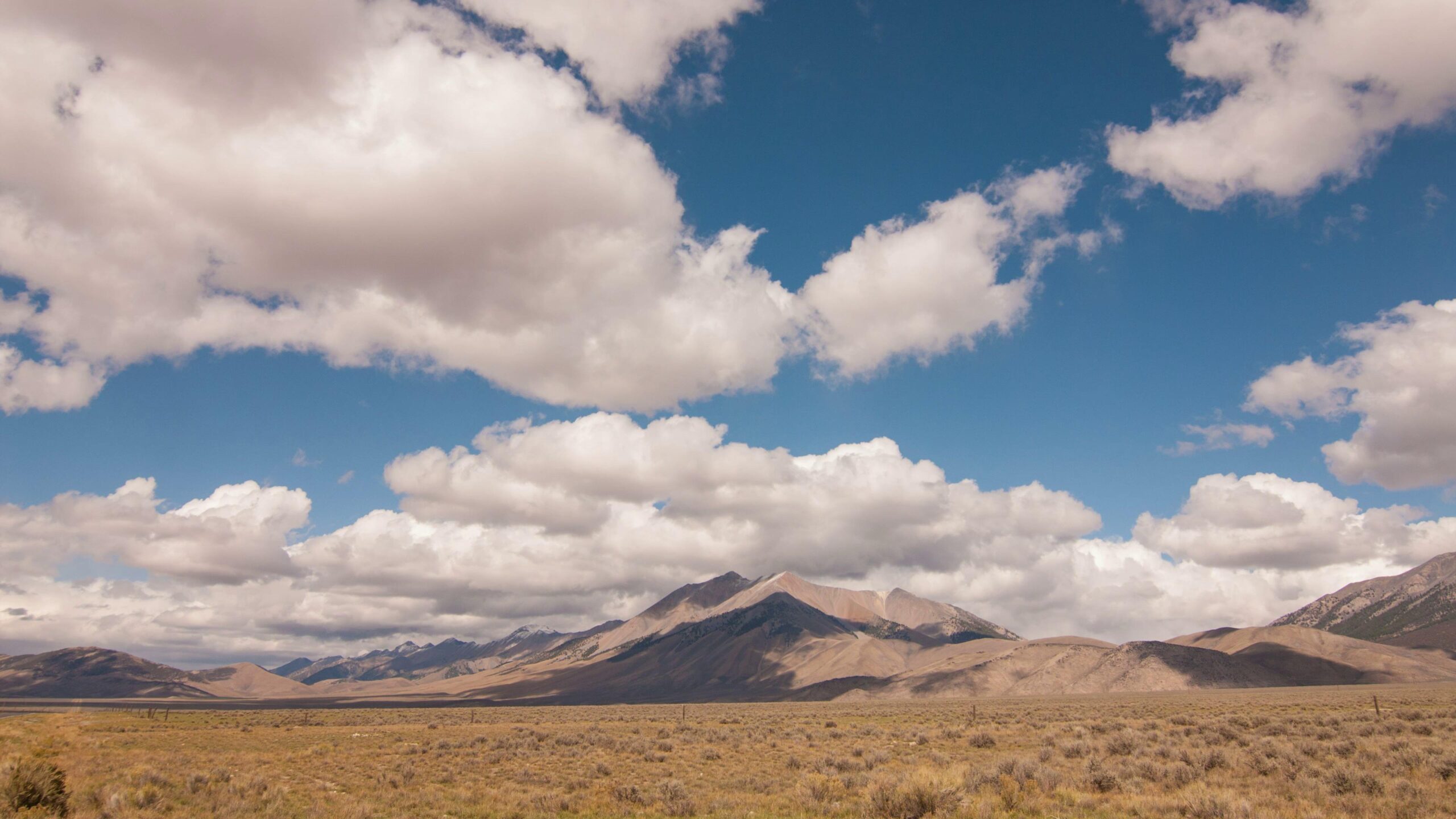 4K video of broad plains and towering mountains beneath a cloud-filled sky display a serene time-lapse landscape.
