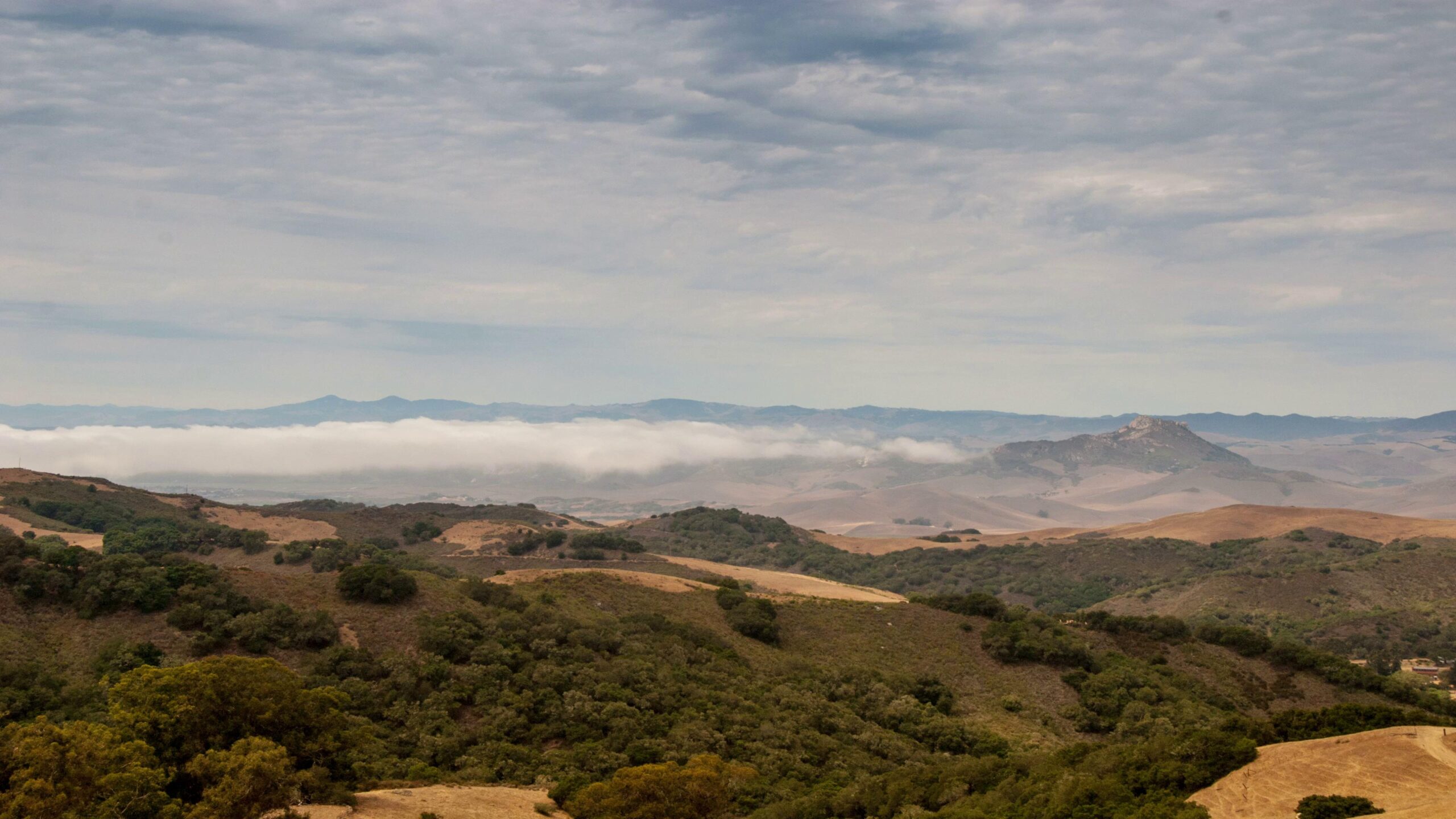 Serene hillside vista with foggy valley and distant mountains under time-lapse cloudy skies.