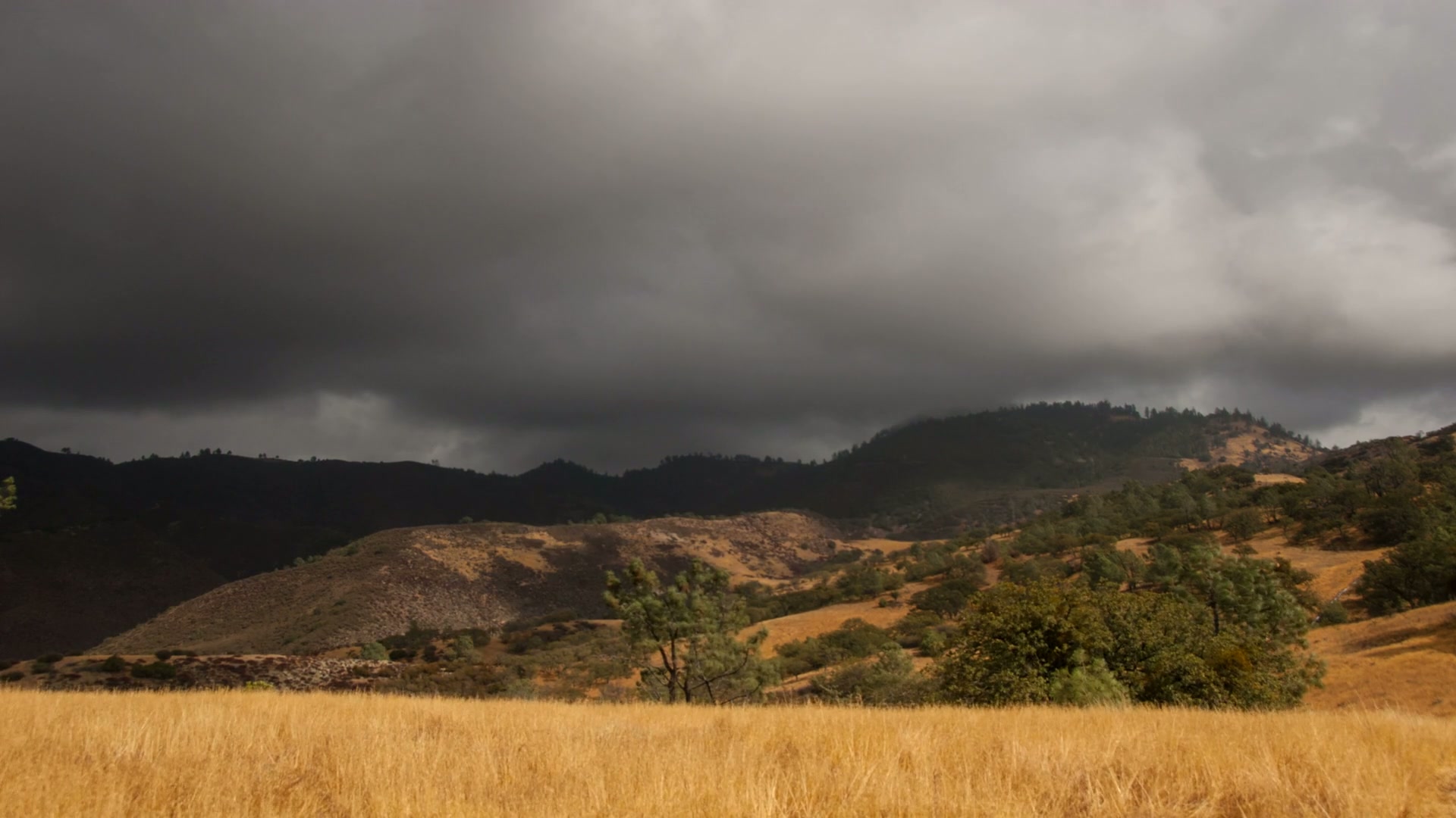 Dark time-lapse storm clouds travel over rural hills and a grassy field landscape.