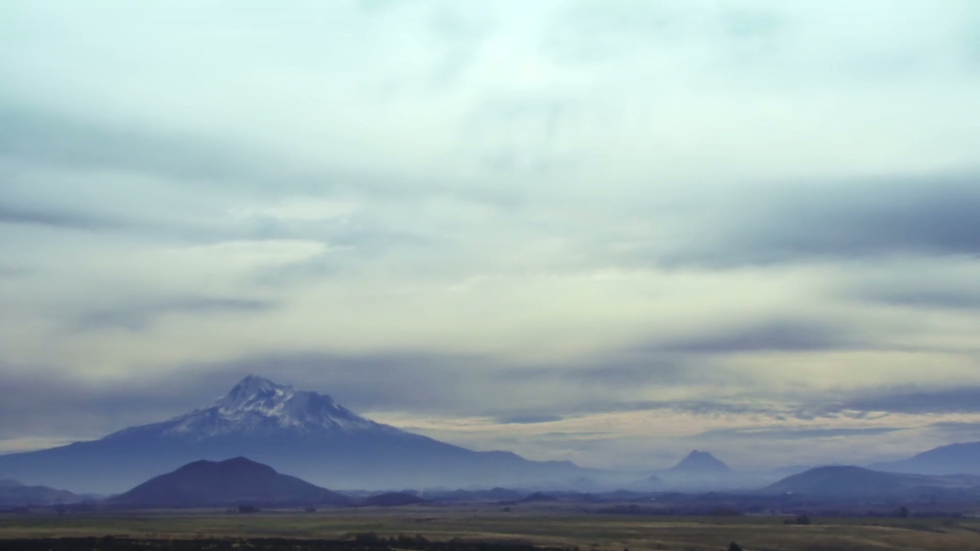 Majestic snow-capped mountain landscape with time-lapse cloudy skies, featuring expansive plains and distant hills under a serene and peaceful atmosphere.