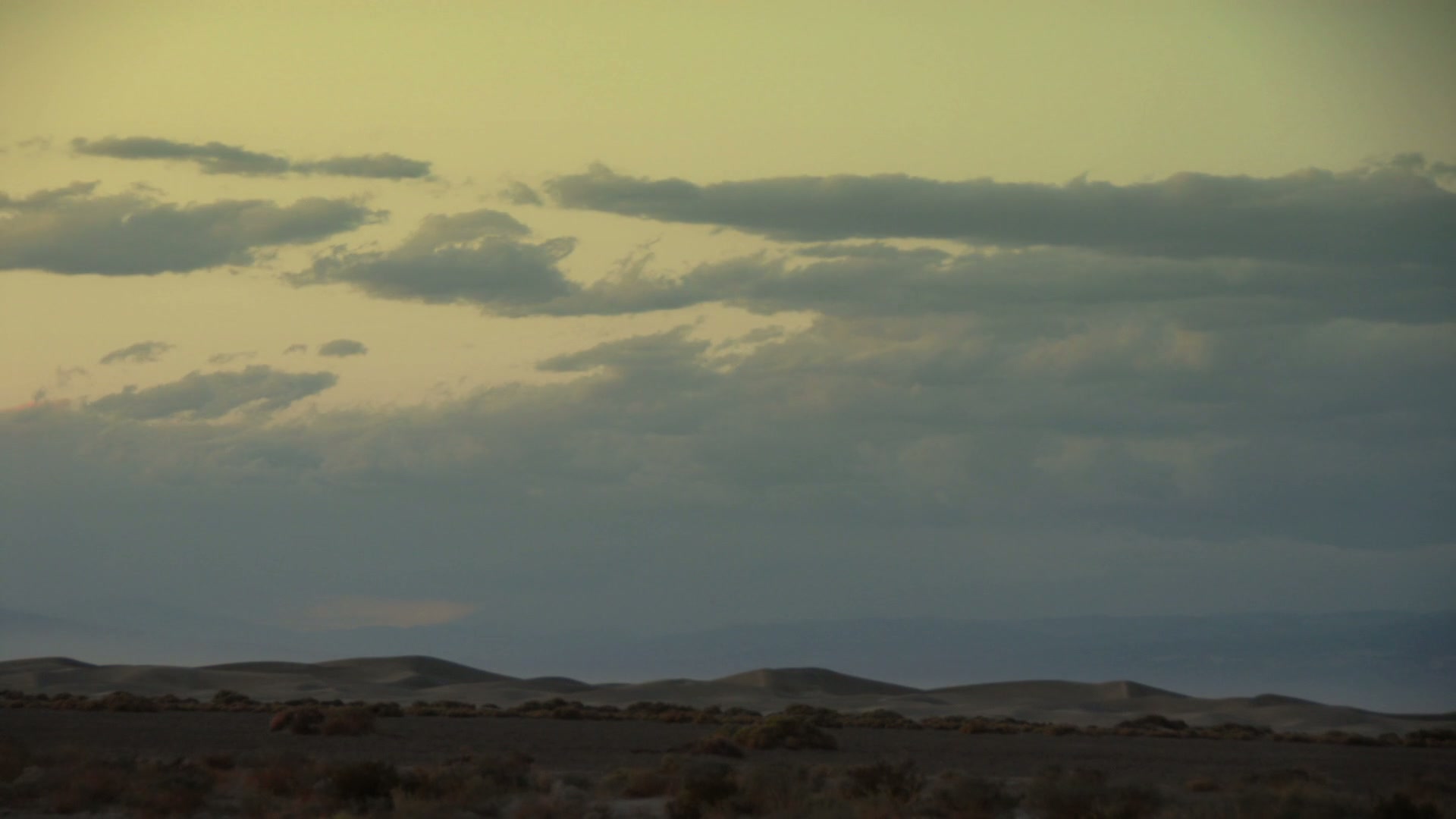 A serene desert landscape with rolling dunes under a time-lapse cloudy sky at dawn or dusk, showcasing natural beauty and tranquility.