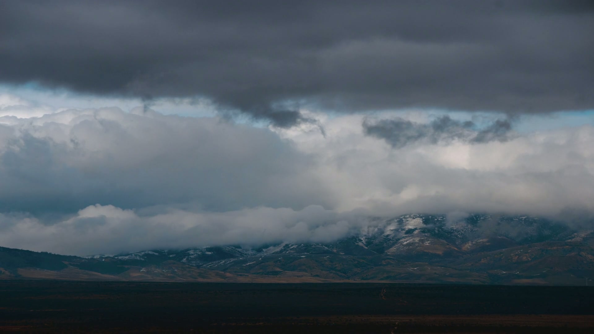 HD video of a dramatic landscape with dark storm clouds hovering over snow-dusted mountain peaks, capturing the raw beauty and power of nature in time-lapse.