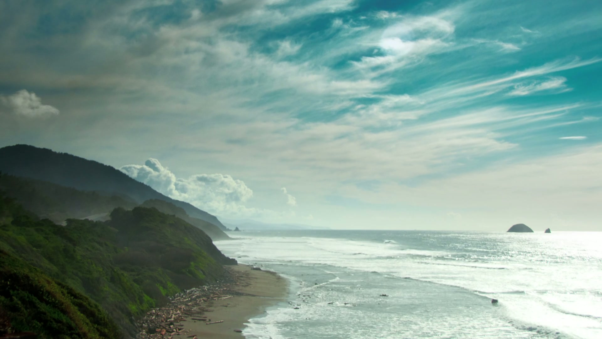 Scenic time-lapse coastal view with green hills and ocean waves.