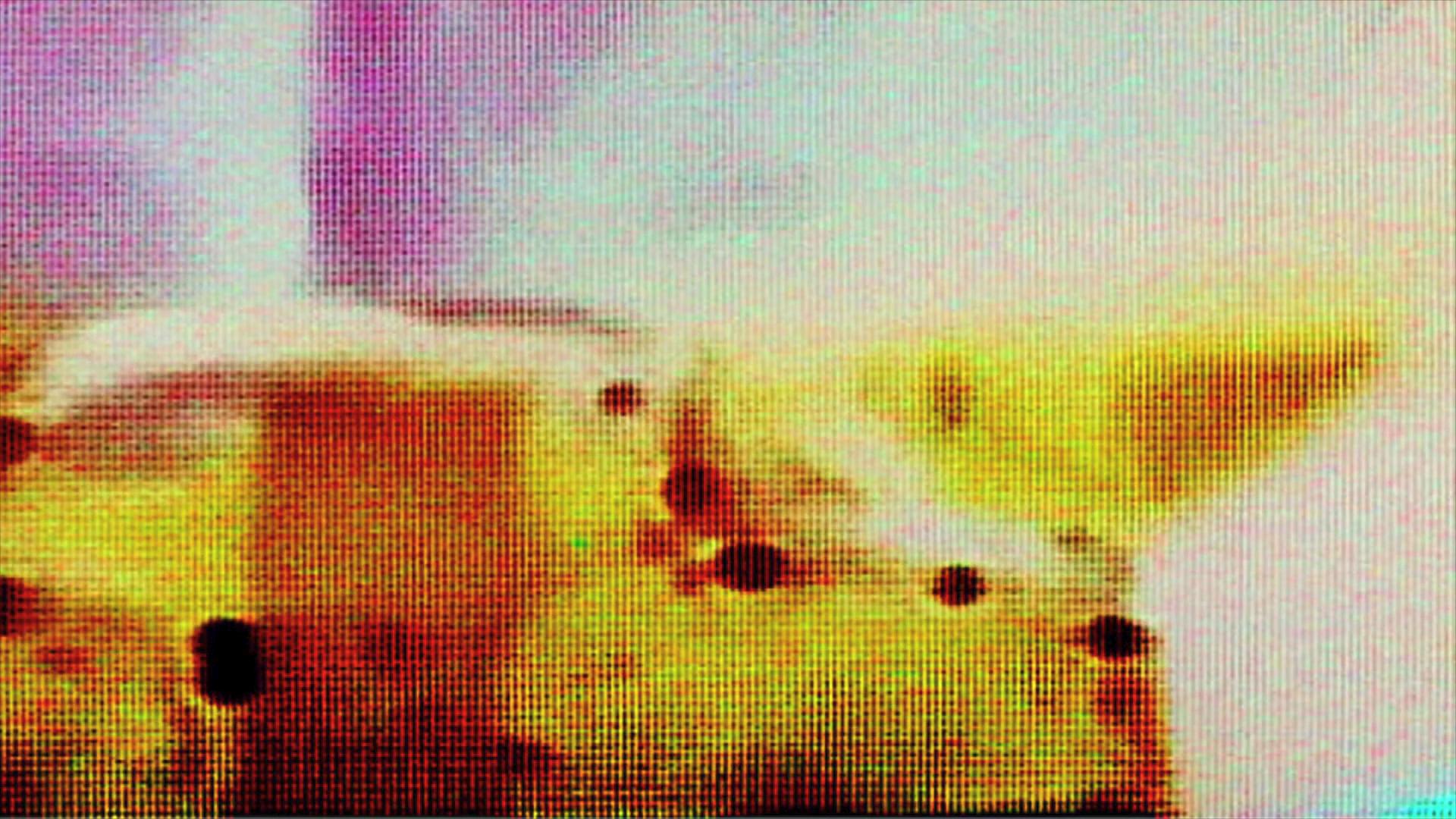 A vivid abstract video loop composed of colorful pixelation featuring dominant yellows and purples with contrasting dark spots scattered across the screen.