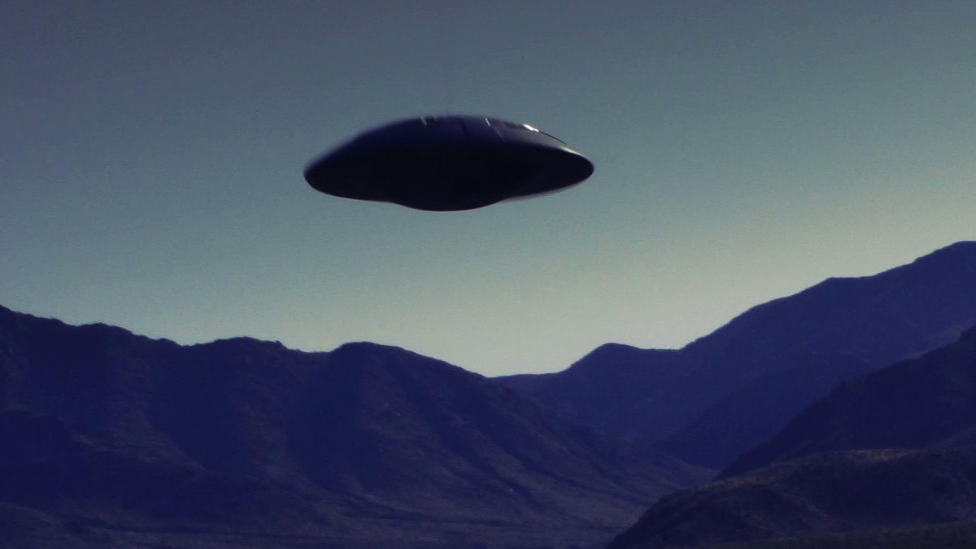 In the video, there is a large, dark object hovering in the sky, resembling a classic UFO or flying saucer.