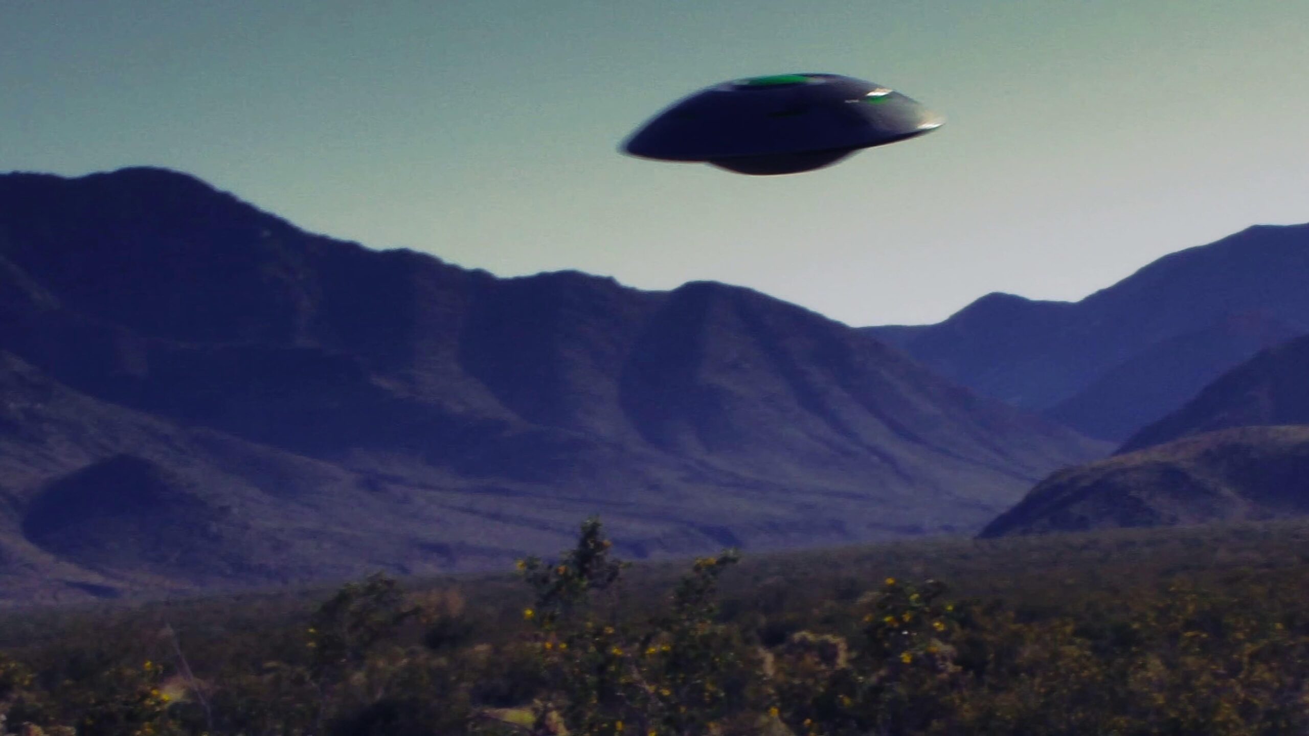Black UFO flies over purple mountains during twilight.