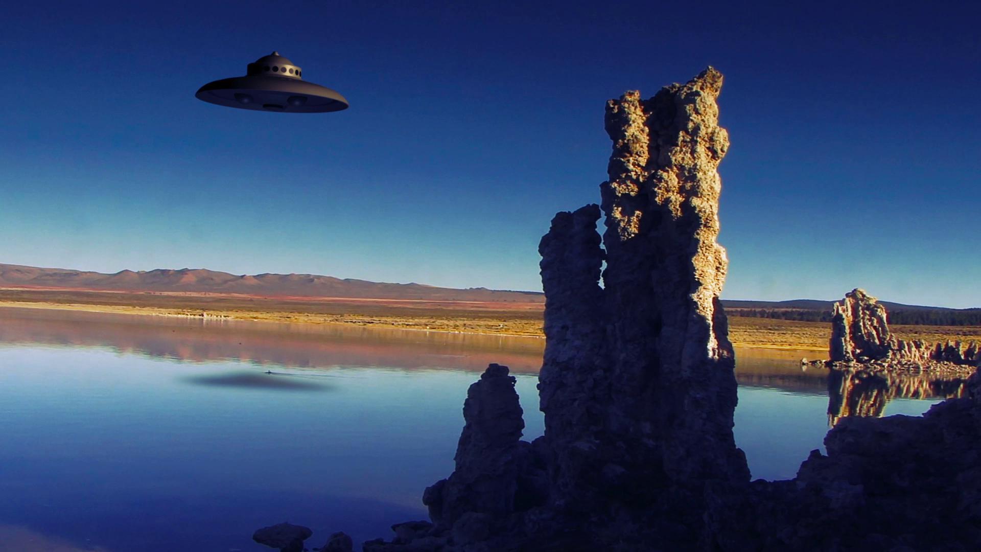 HD video of an alien spacecraft hovering over a serene lake with rocky formations in a scenic landscape.