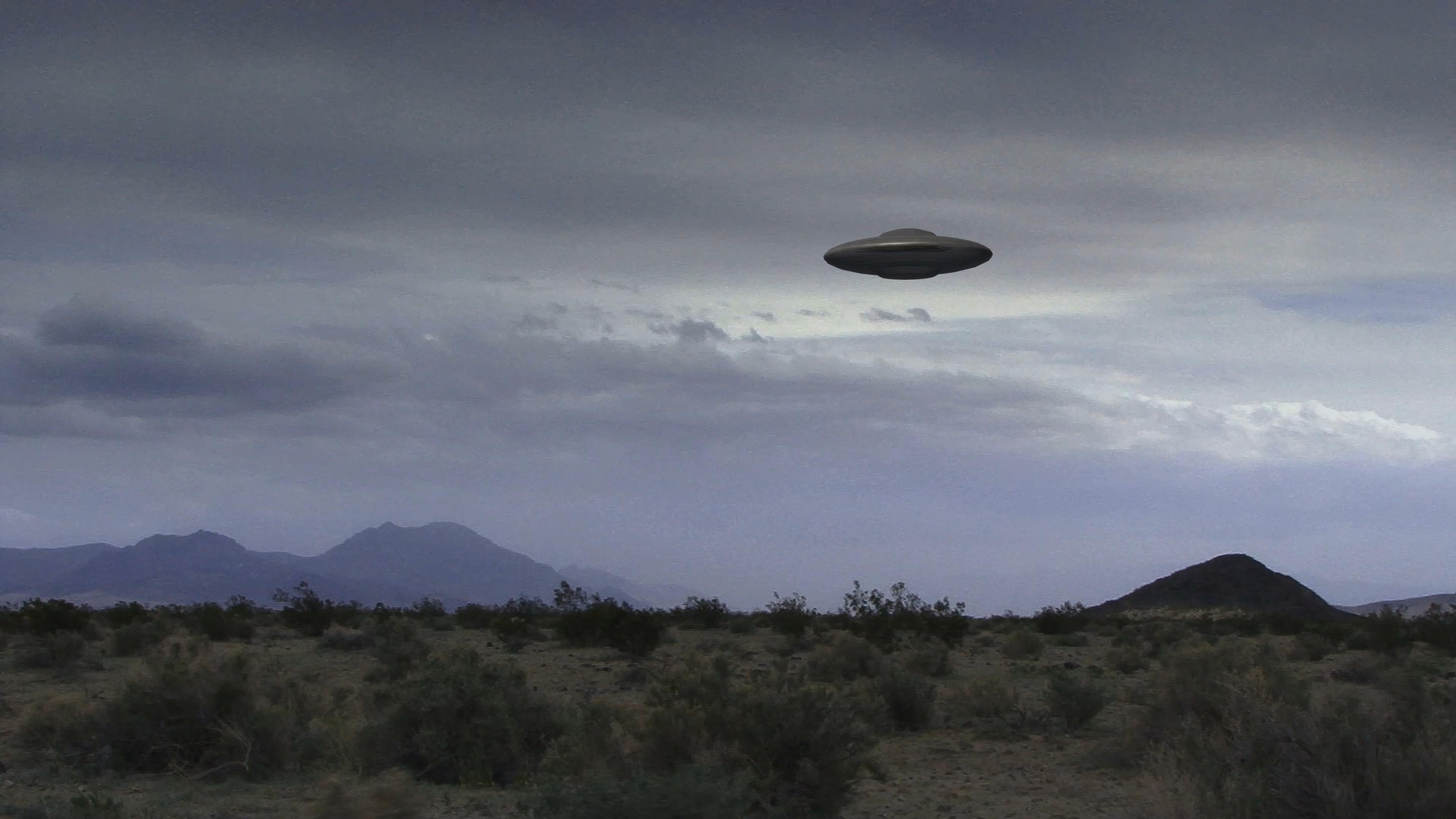 Alien spacecraft hovers silently over barren desert mountainscape during twilight hour.