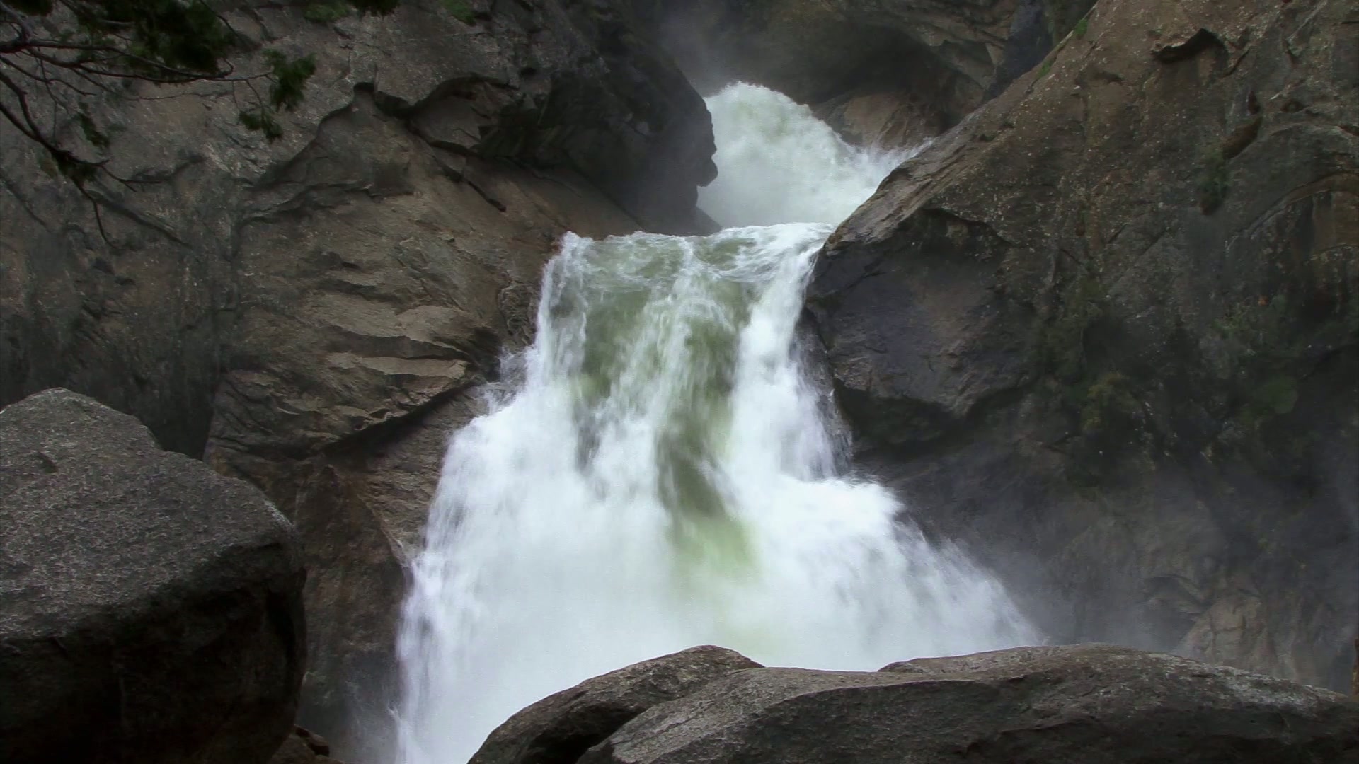 Powerful waterfall cascading over rugged rocks with mist rising, set amidst a natural, untouched landscape.