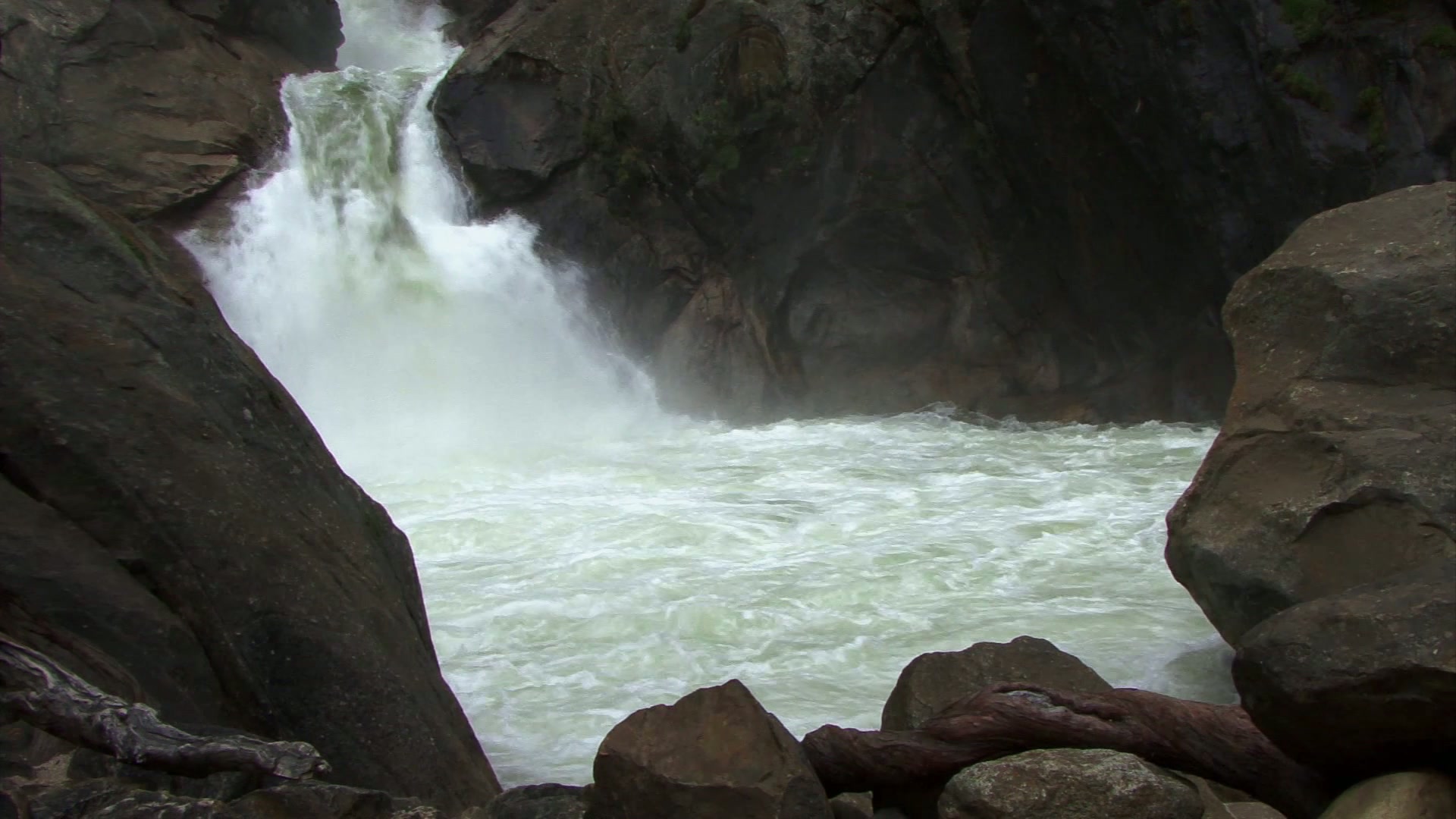 Powerful waterfall cascading over rugged rocks surrounded by a natural wilderness, with mist rising from the frothy water below.
