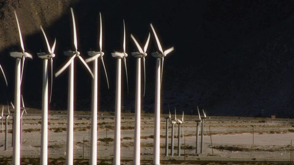 Wind turbines in a desert landscape against a mountain backdrop, highlighting clean energy and sustainable technology in an arid environment.