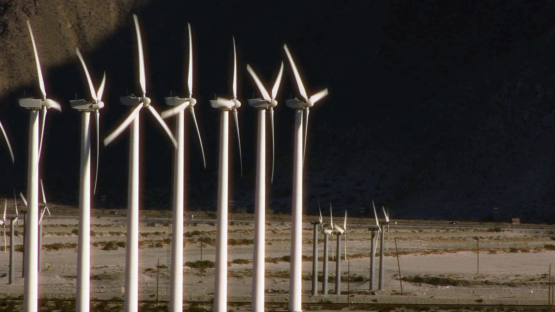 Wind turbines in a desert landscape against a mountain backdrop, highlighting clean energy and sustainable technology in an arid environment.