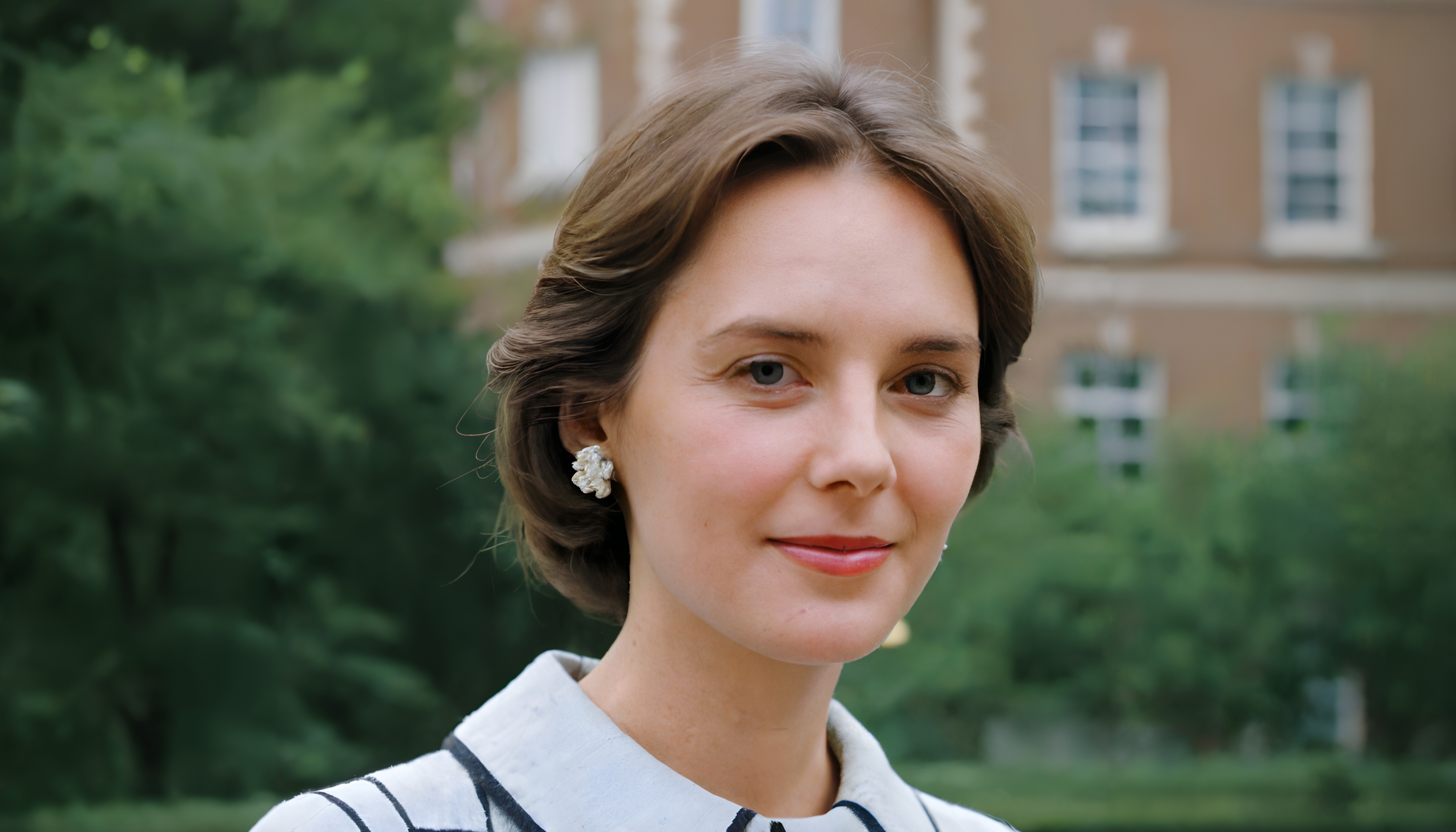 Portrait of a woman with short brown hair, wearing a white top, in front of a brick building.