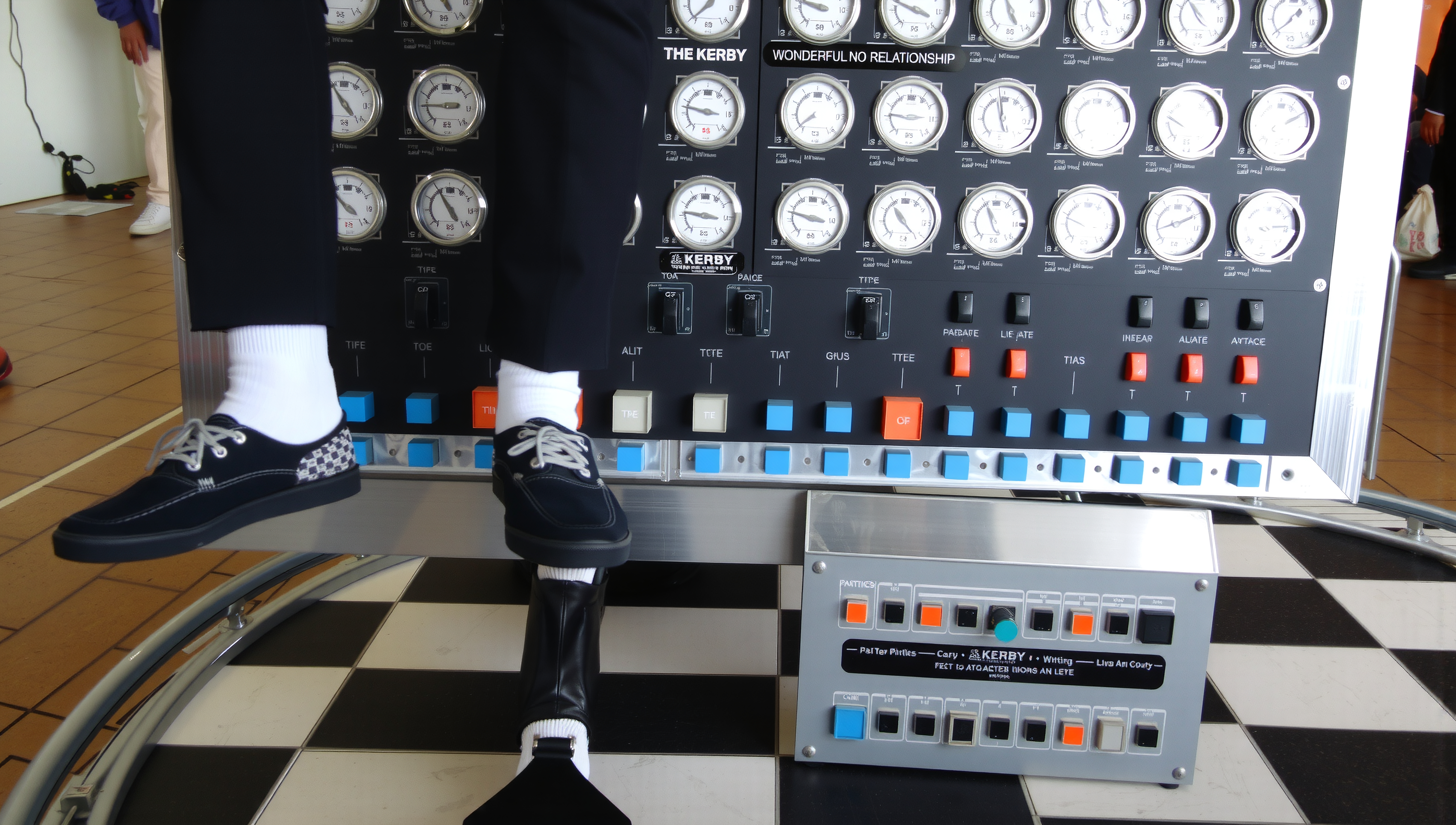 A person sitting on a complex control panel displaying numerous dials and switches in an indoor setting.
