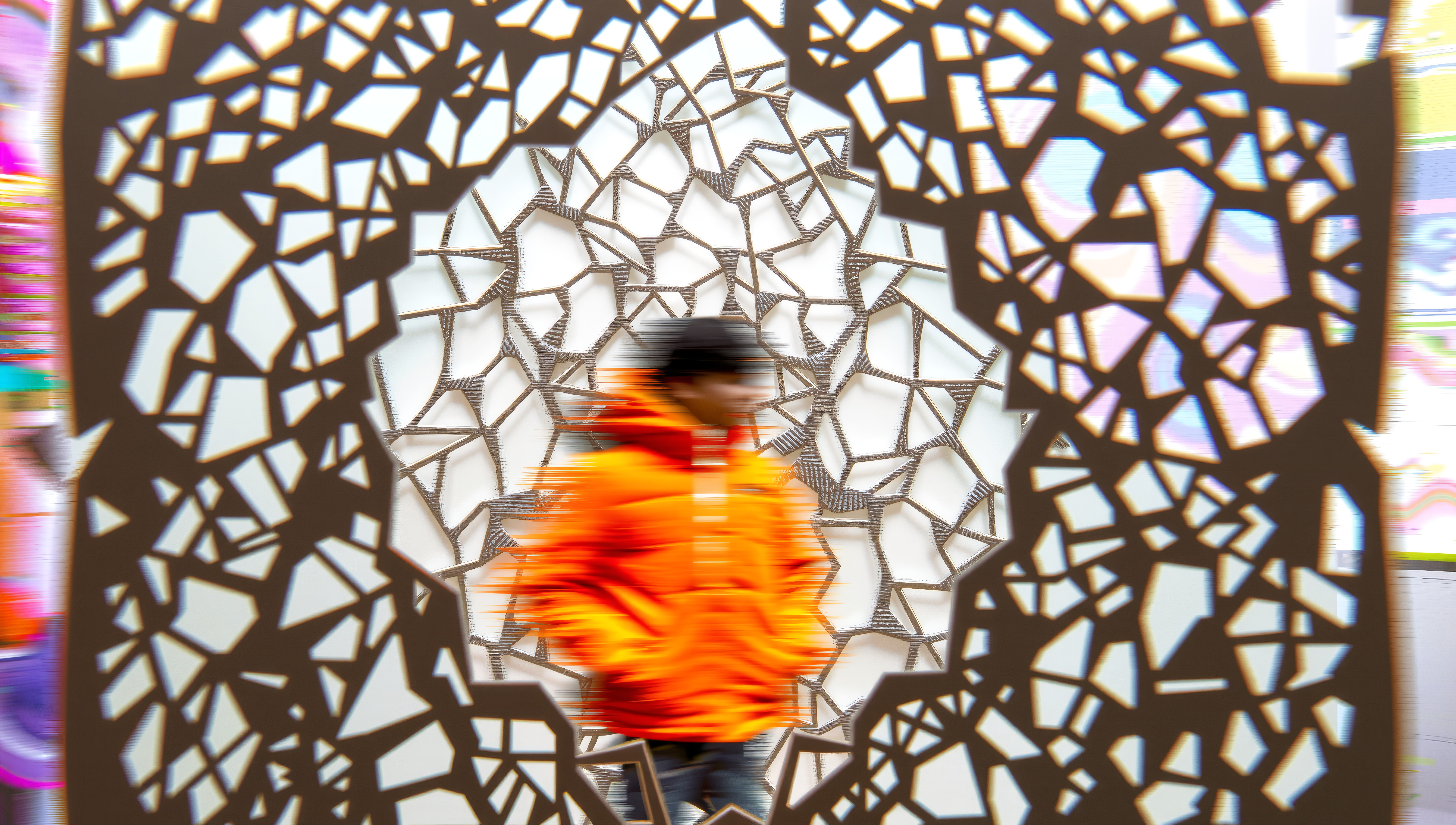Person in orange jacket, standing against a geometric patterned background.