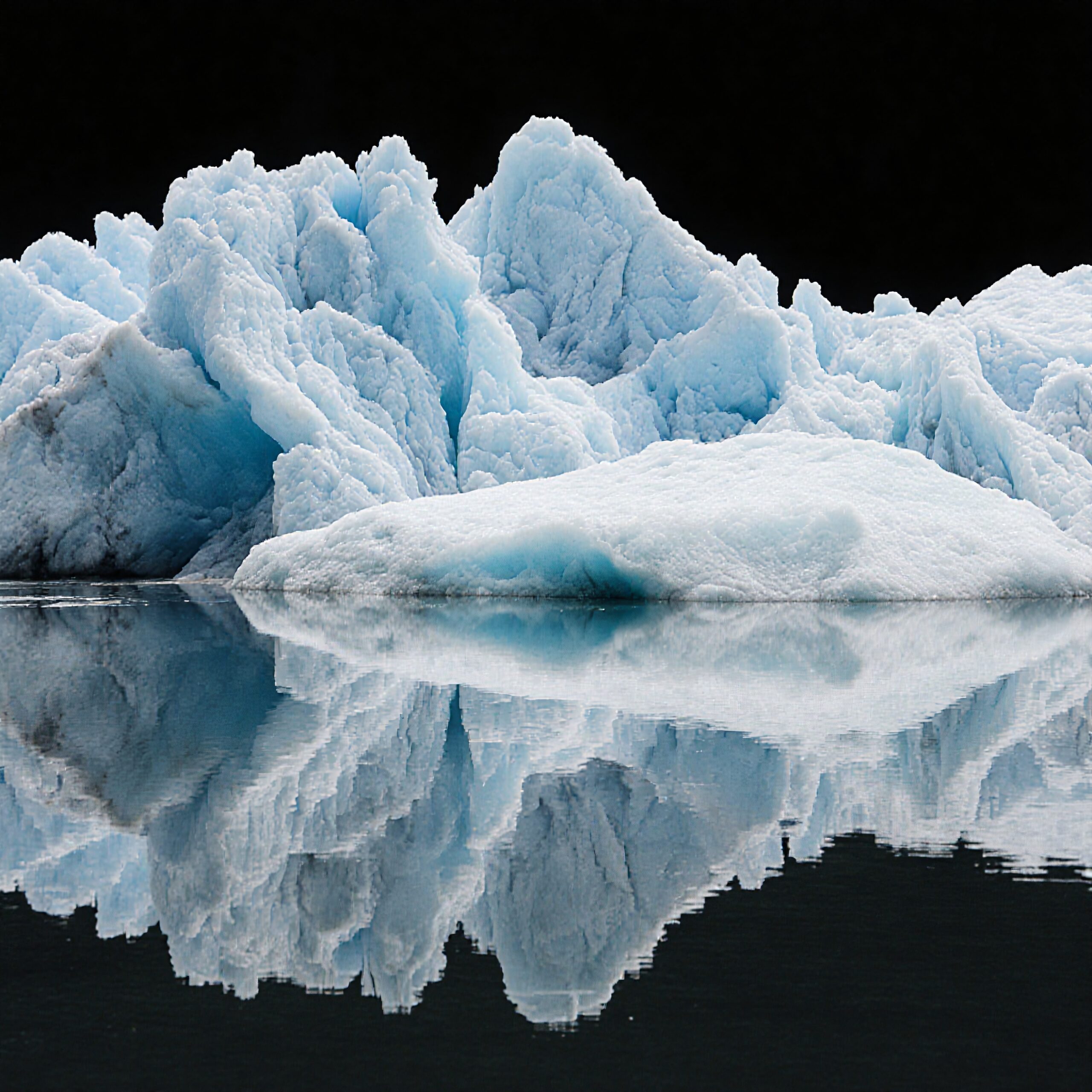 A towering blue iceberg reflecting in calm, dark waters, creating a dramatic and serene natural scene.