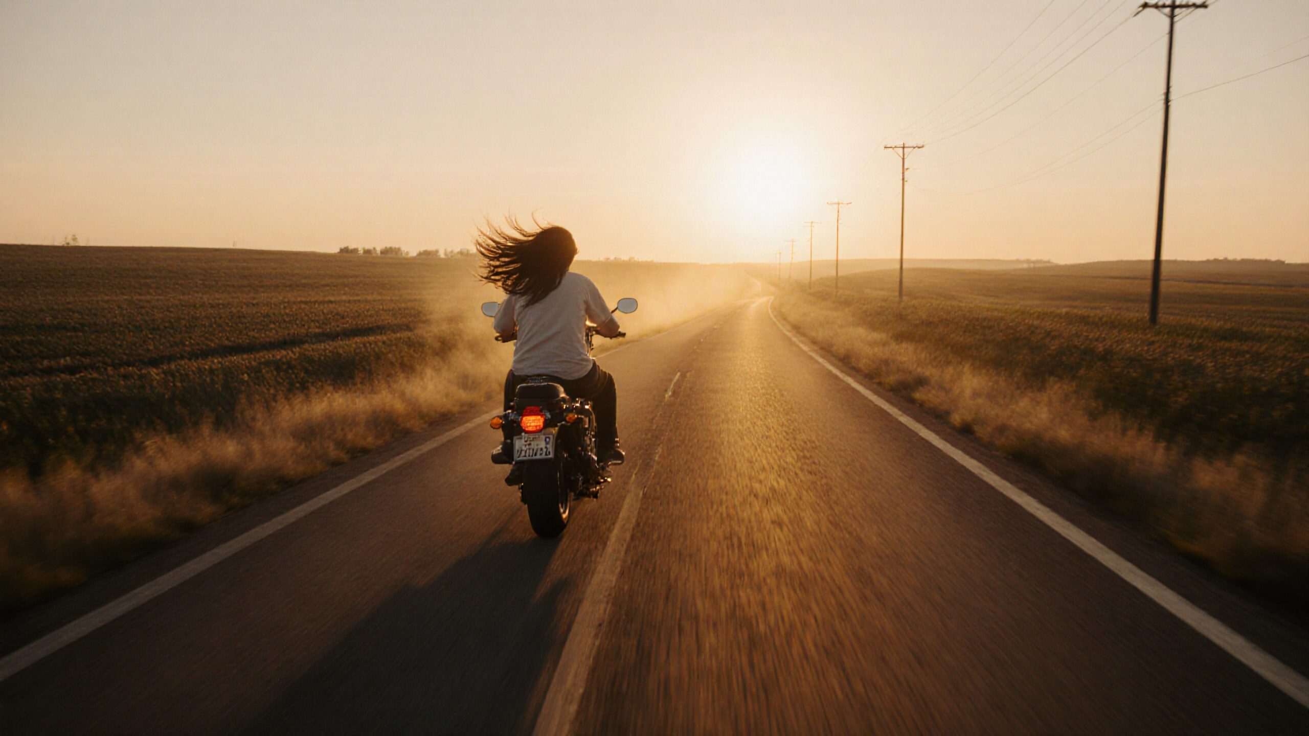 A motorcyclist rides alone on an open road at sunset.