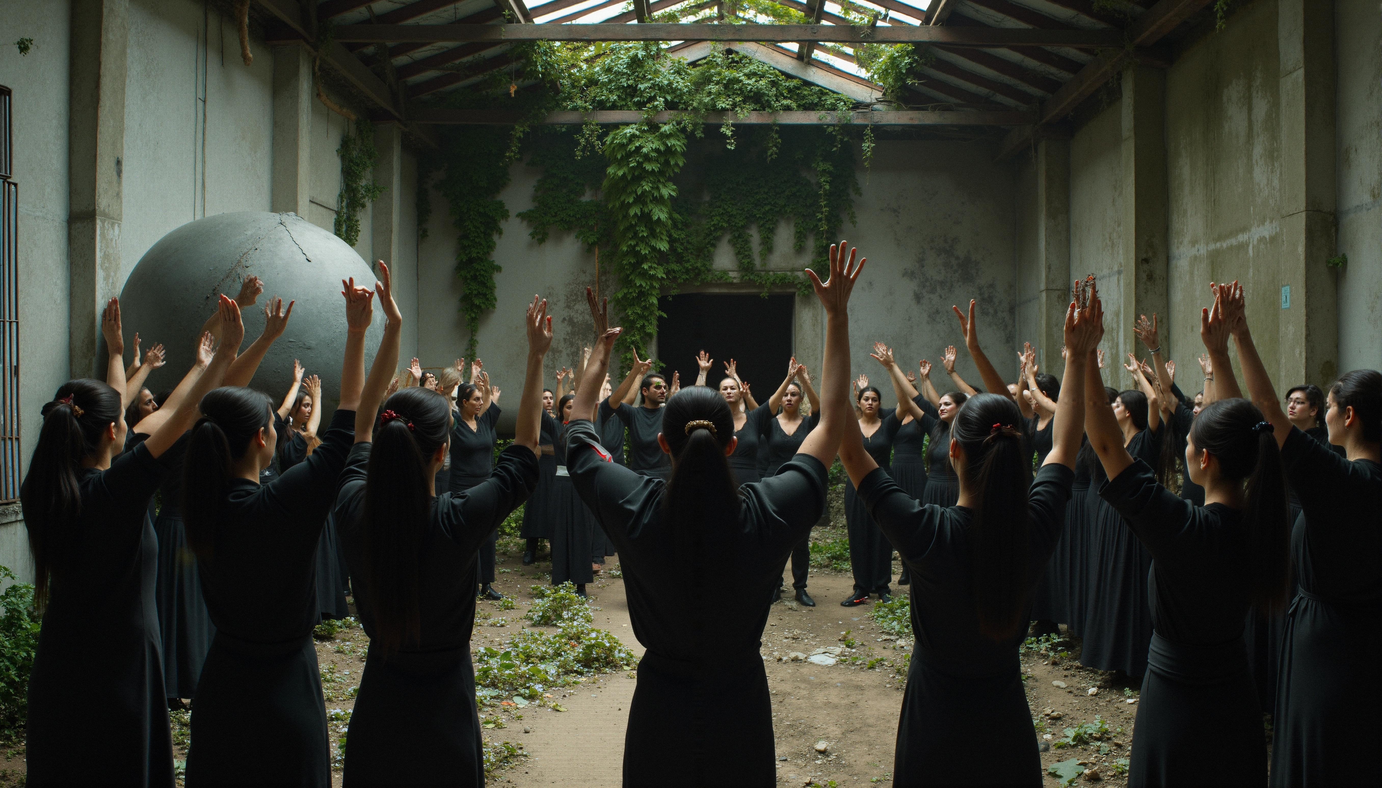A group raises arms in a circle under a glass, plant-lined roof.